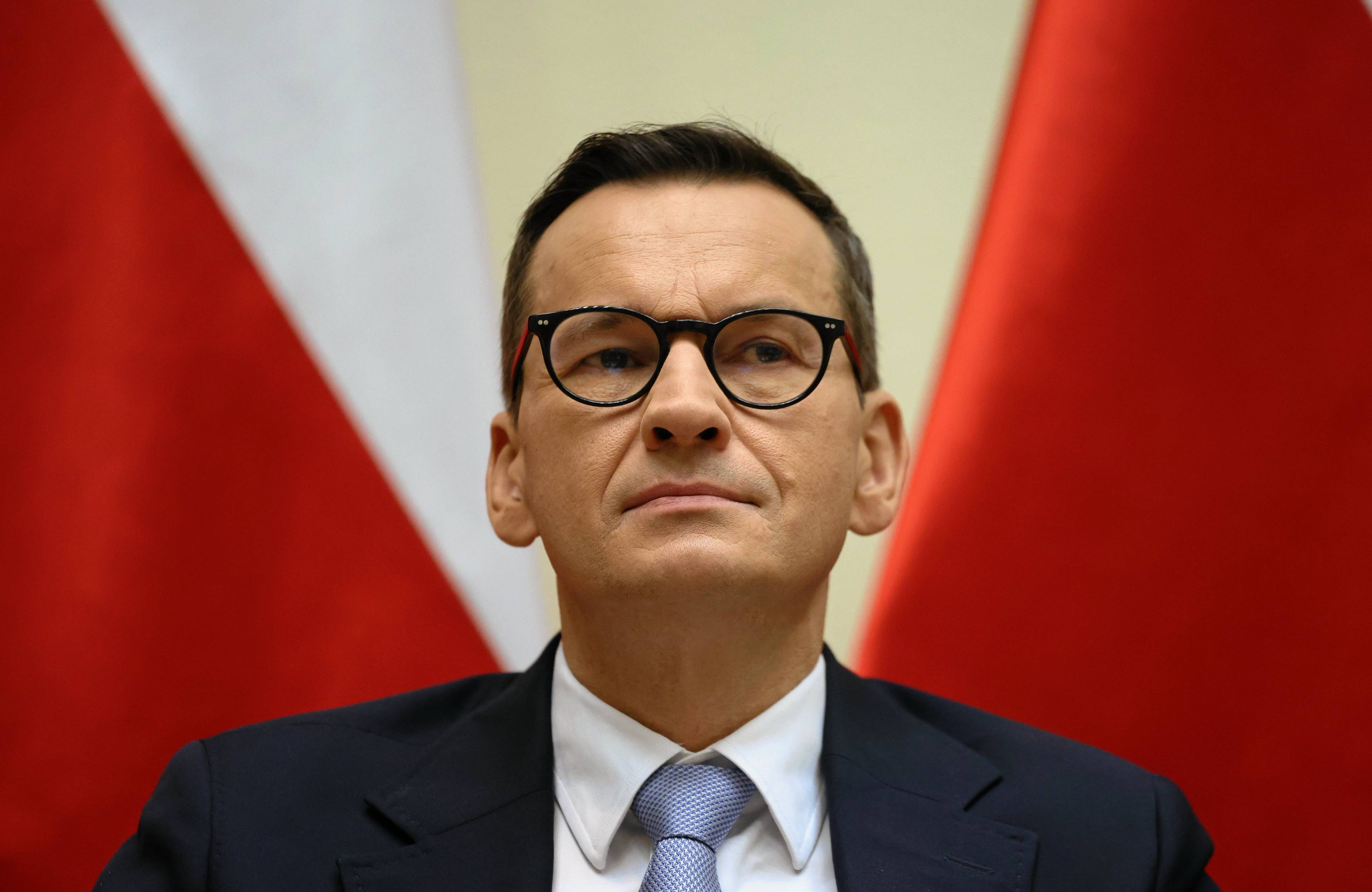 Mateusz Morawiecki na tle flag Polski