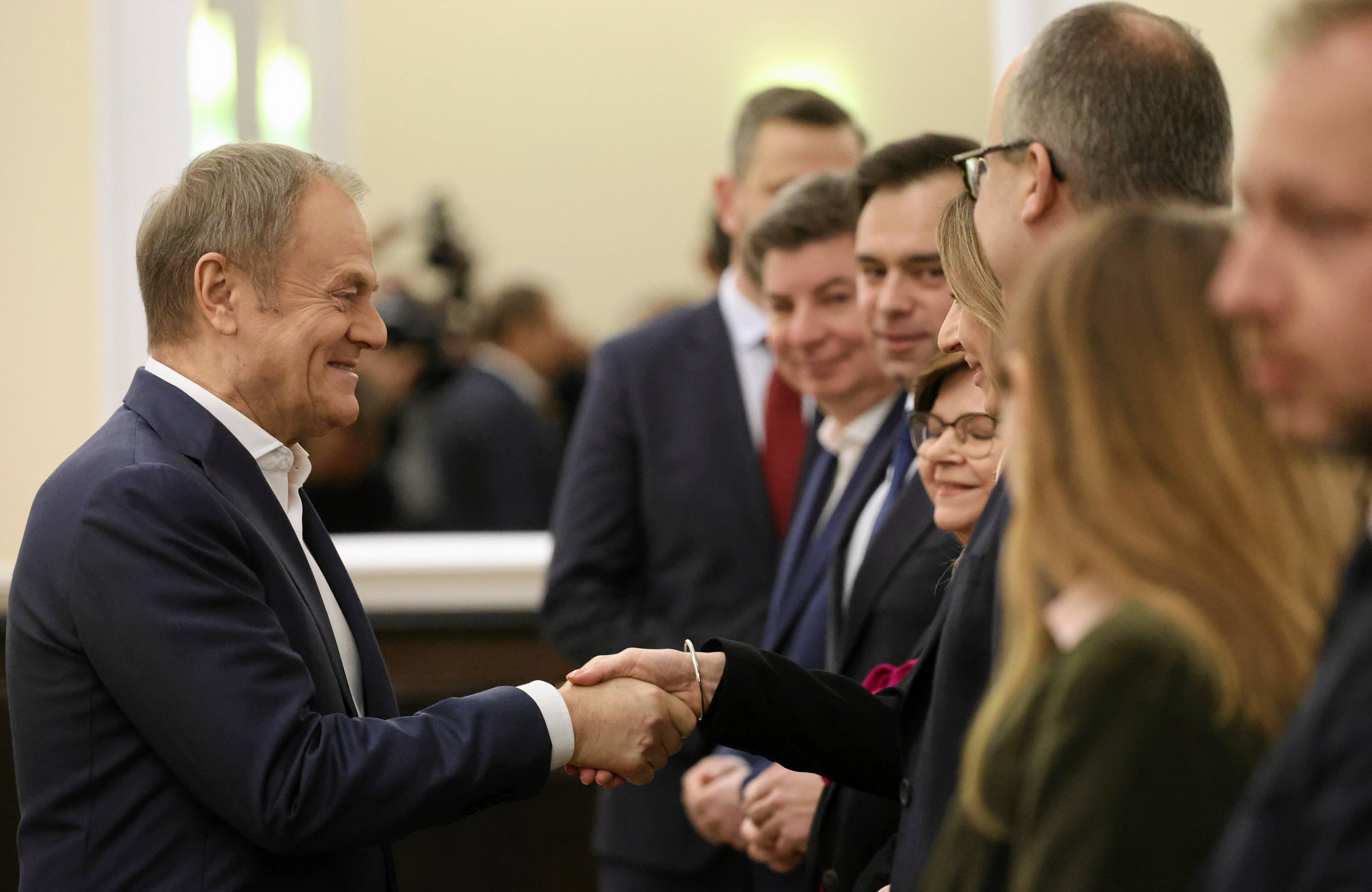 Donald Tusk uśmiecha się i ściska dłoń jednego z ministrów