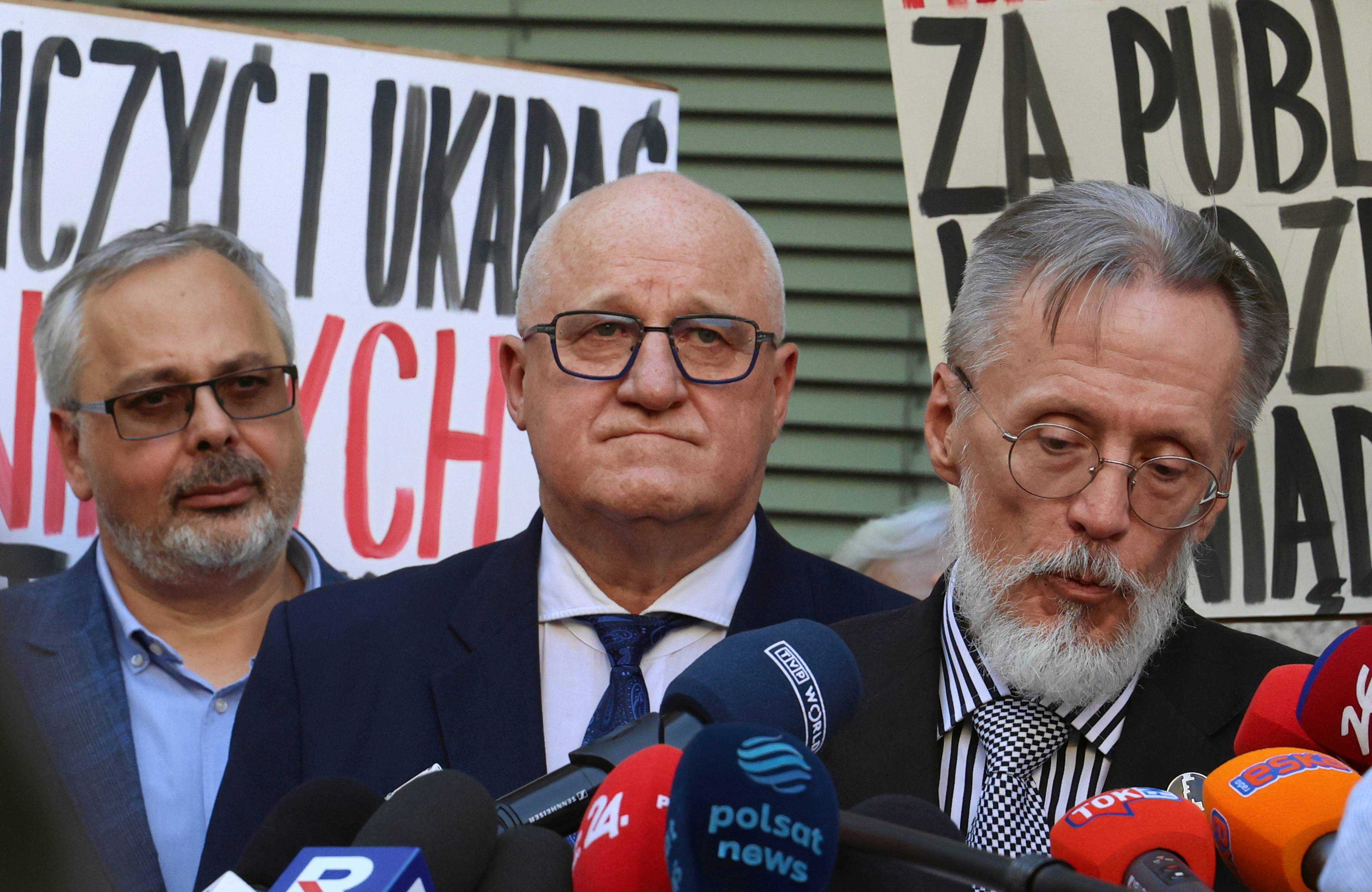 Trzech mężczyzn przed mikrofonem, w tle protest