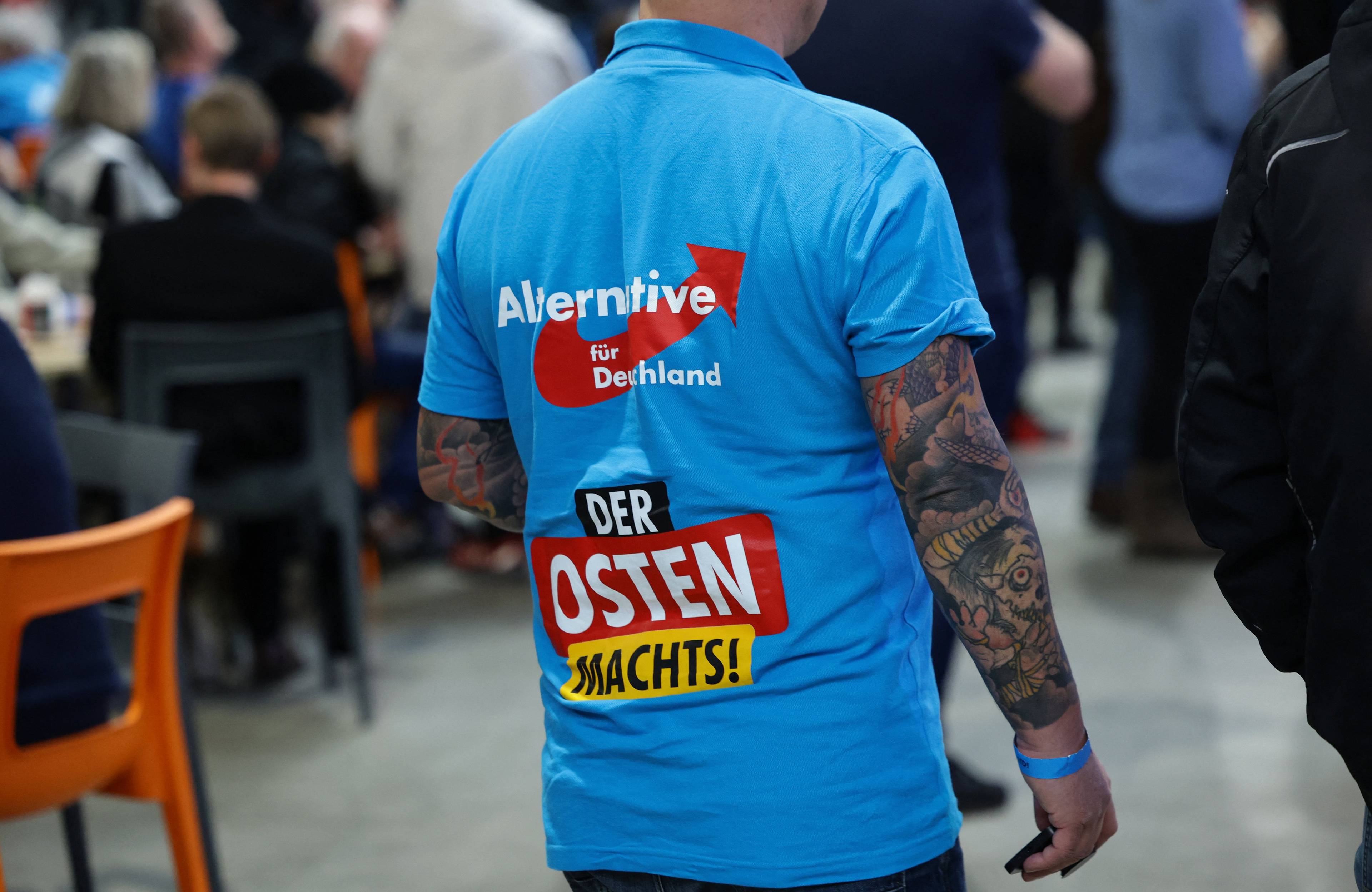 Mężczyzna w tatuażach w niebieskiej koszulce z napisem Alternative fur Deutschland