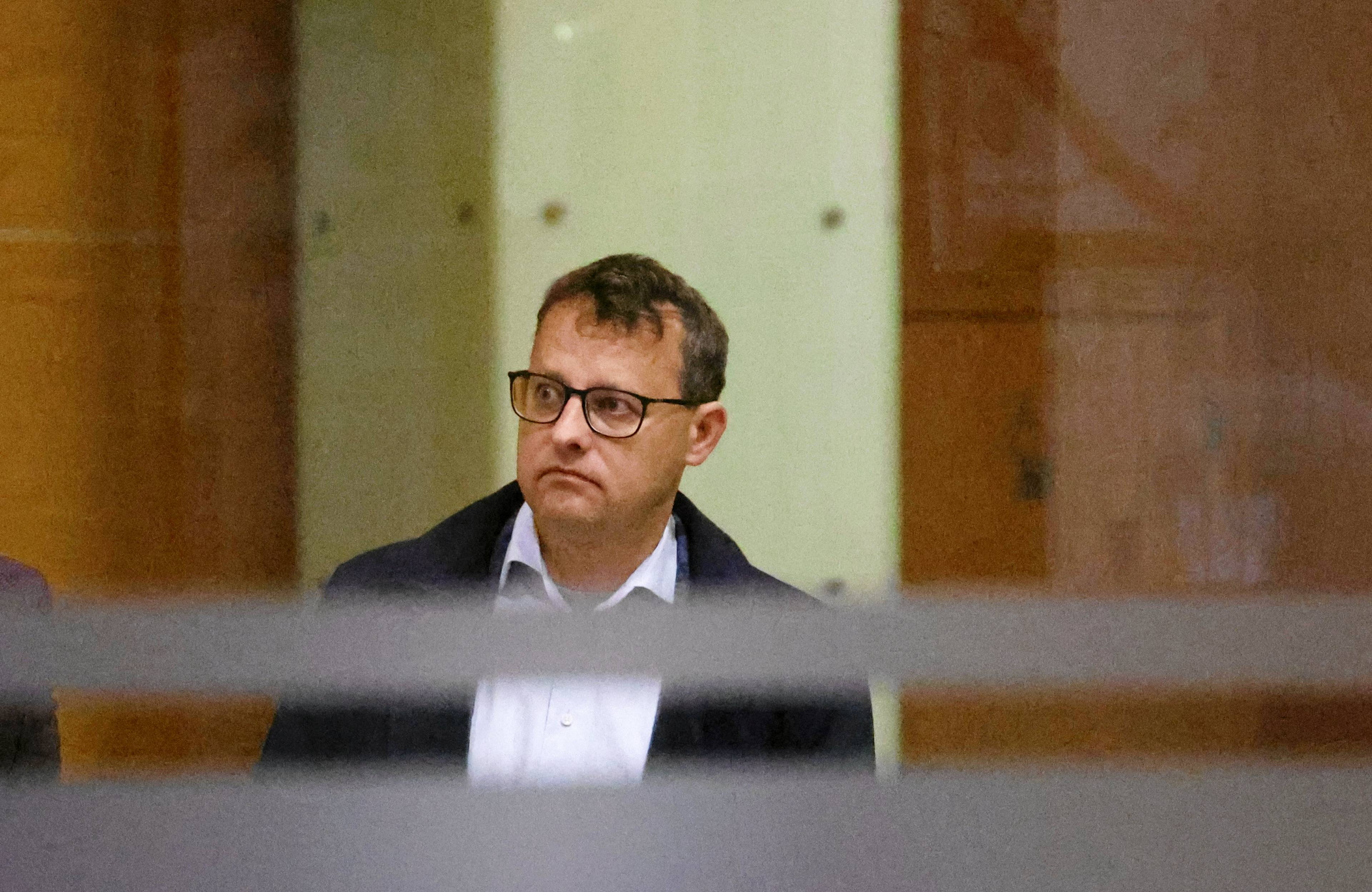 Mężczyzna w białej koszuli i płaszczu (Marcin Romanowski) sfotografowany przez szybę witryny