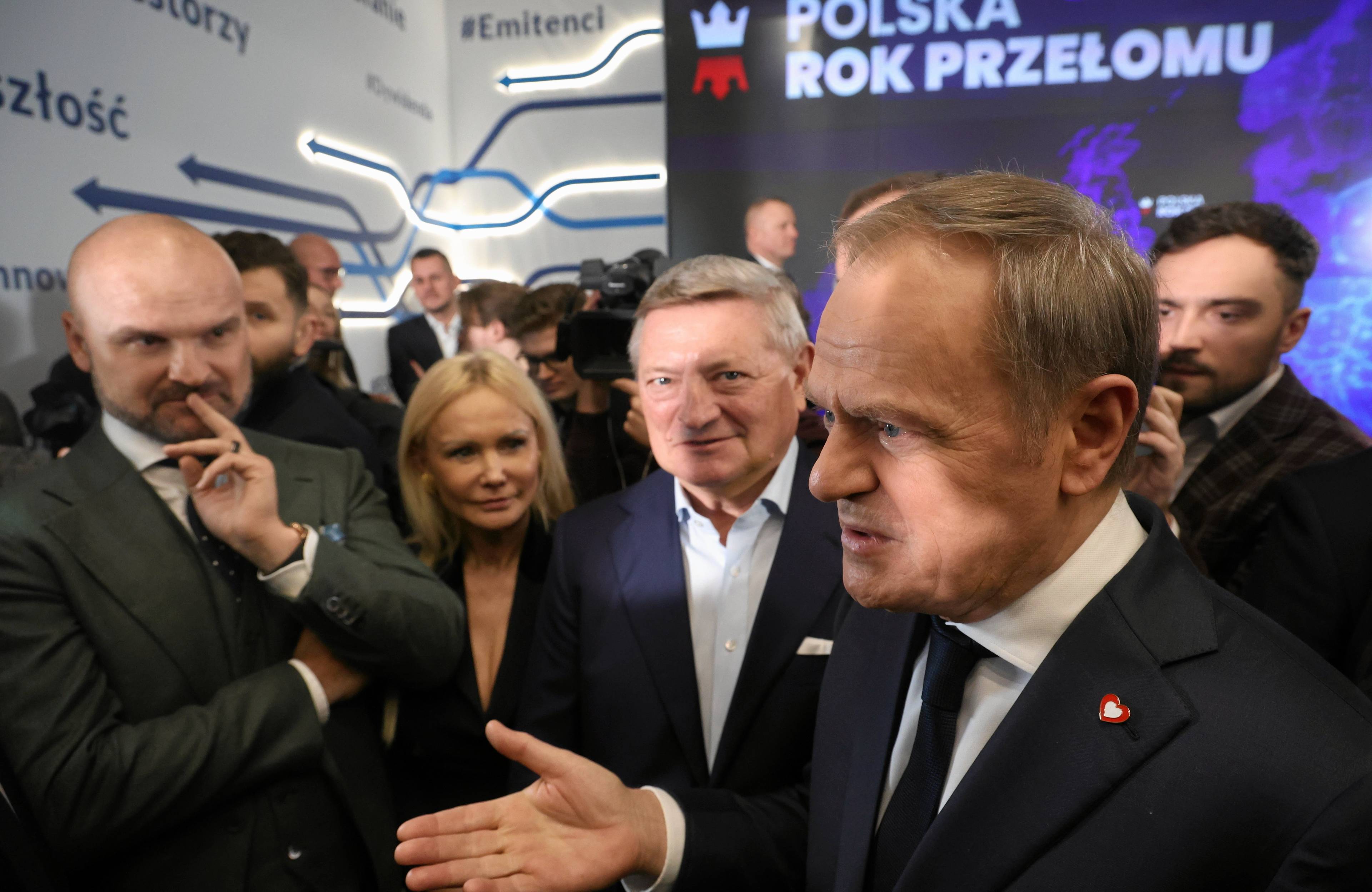 Kilku męzczyzn w garniturach, w tle napis na ścianie Rok przełomu
