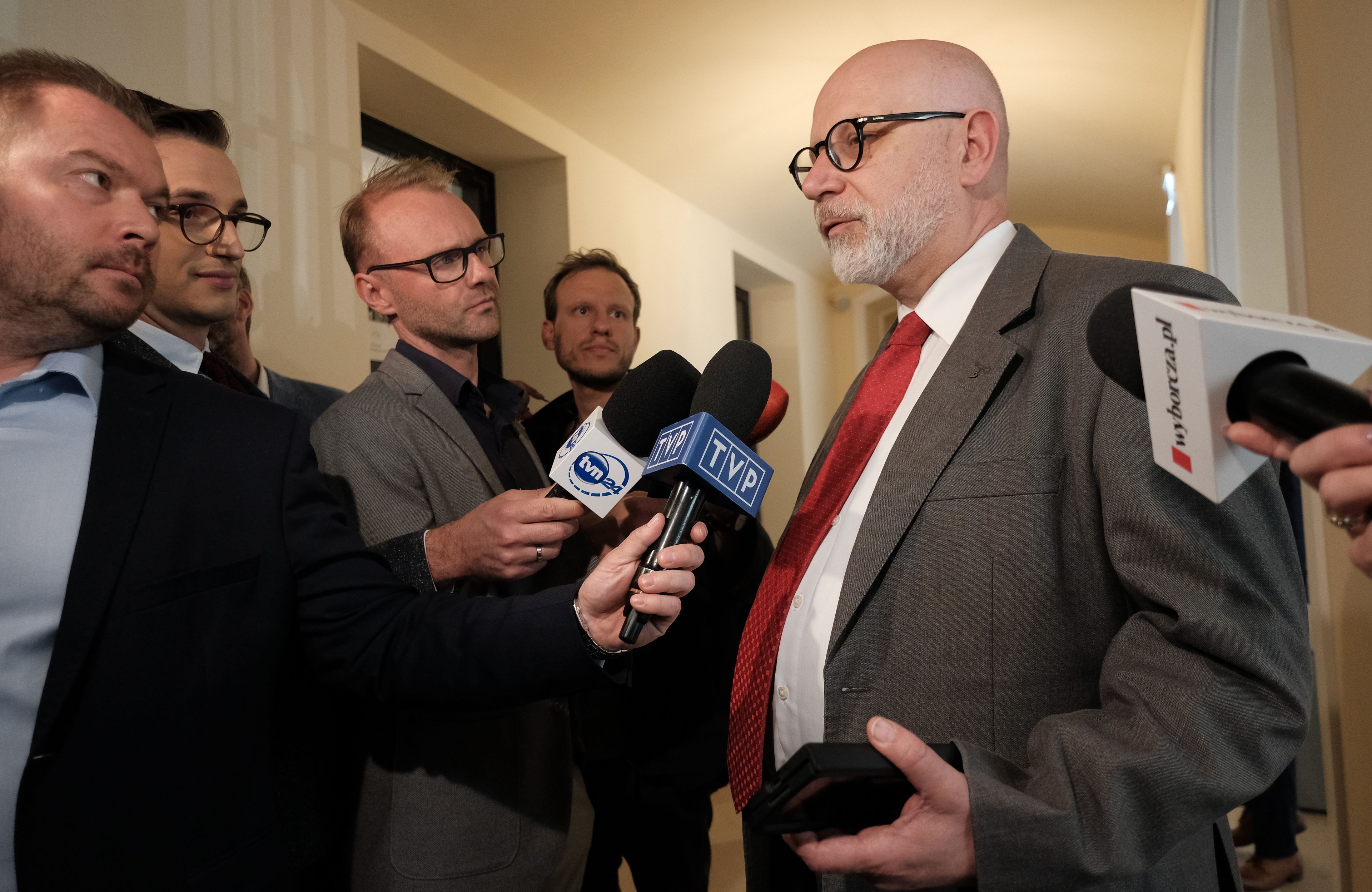 Srarszy męzczyzna odpowiada dziennikarzom. Na pierwszym planie pracownik TVP