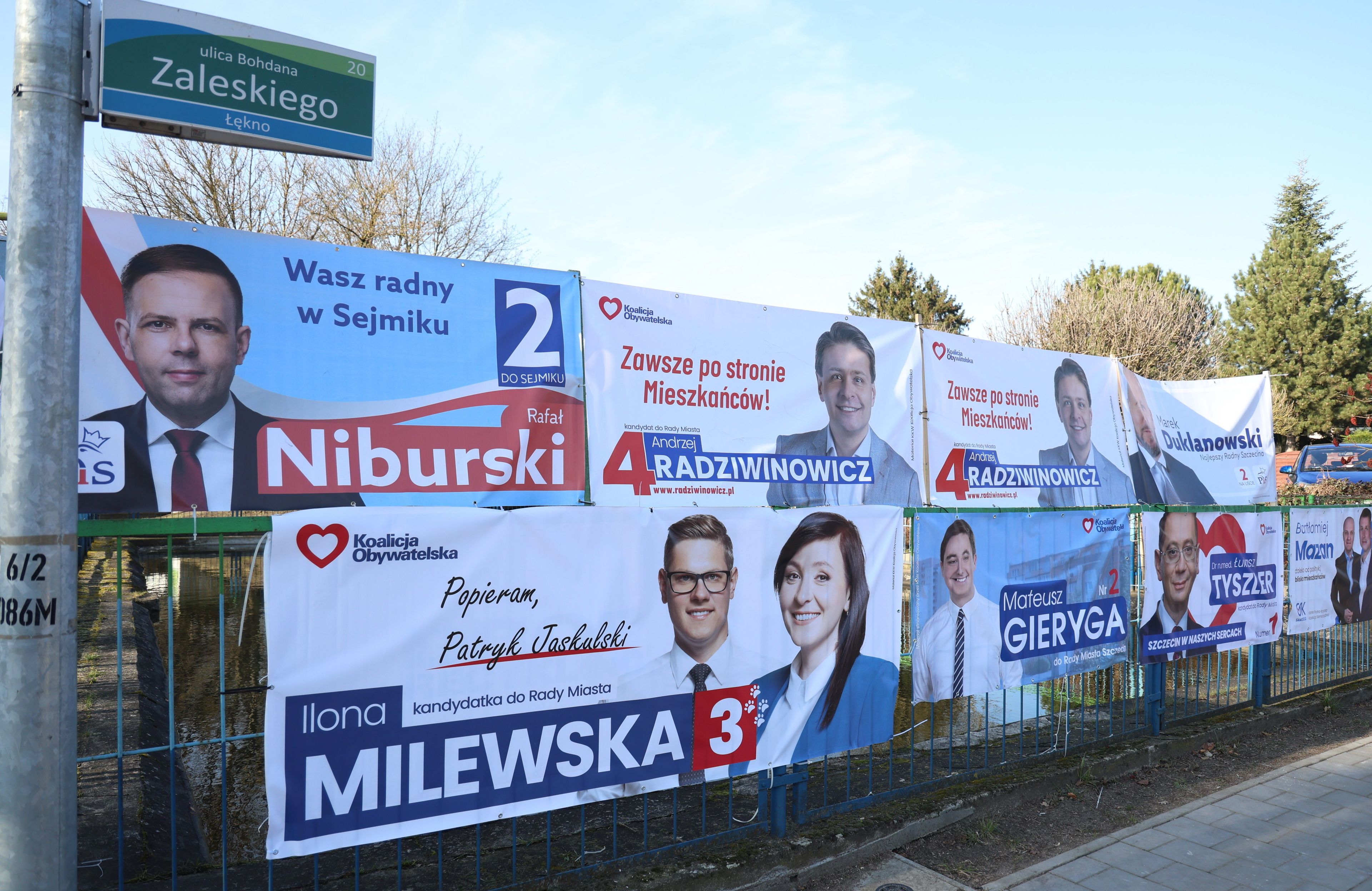Wiszące na płocie plakaty wyborcze kandydatów w wyborach samorządowych, głównie z PiS i KO. Samorząd wybory