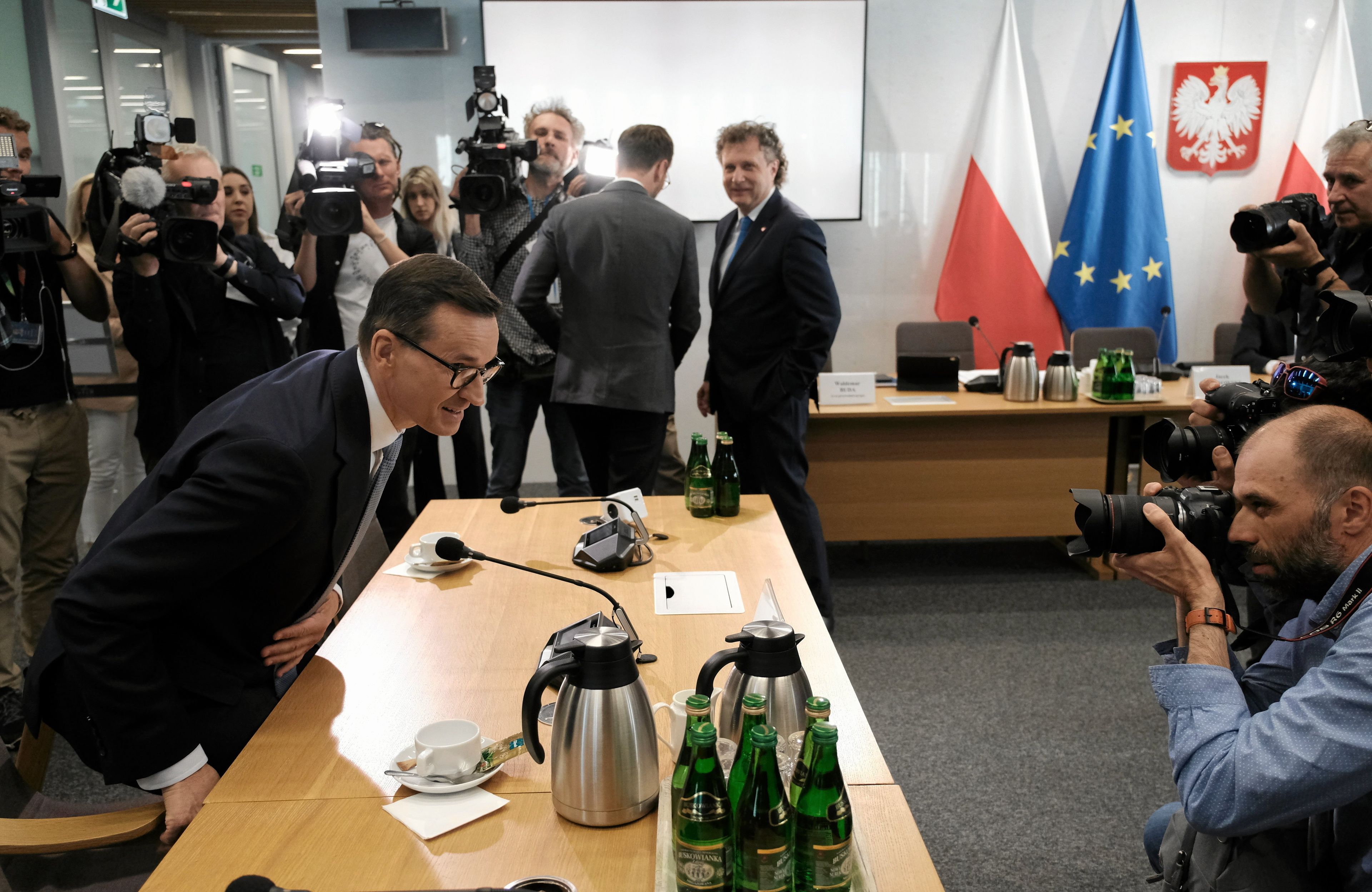 Mateusz Morawiecki siada na krześle, otaczają go posłowie i dziennikarze