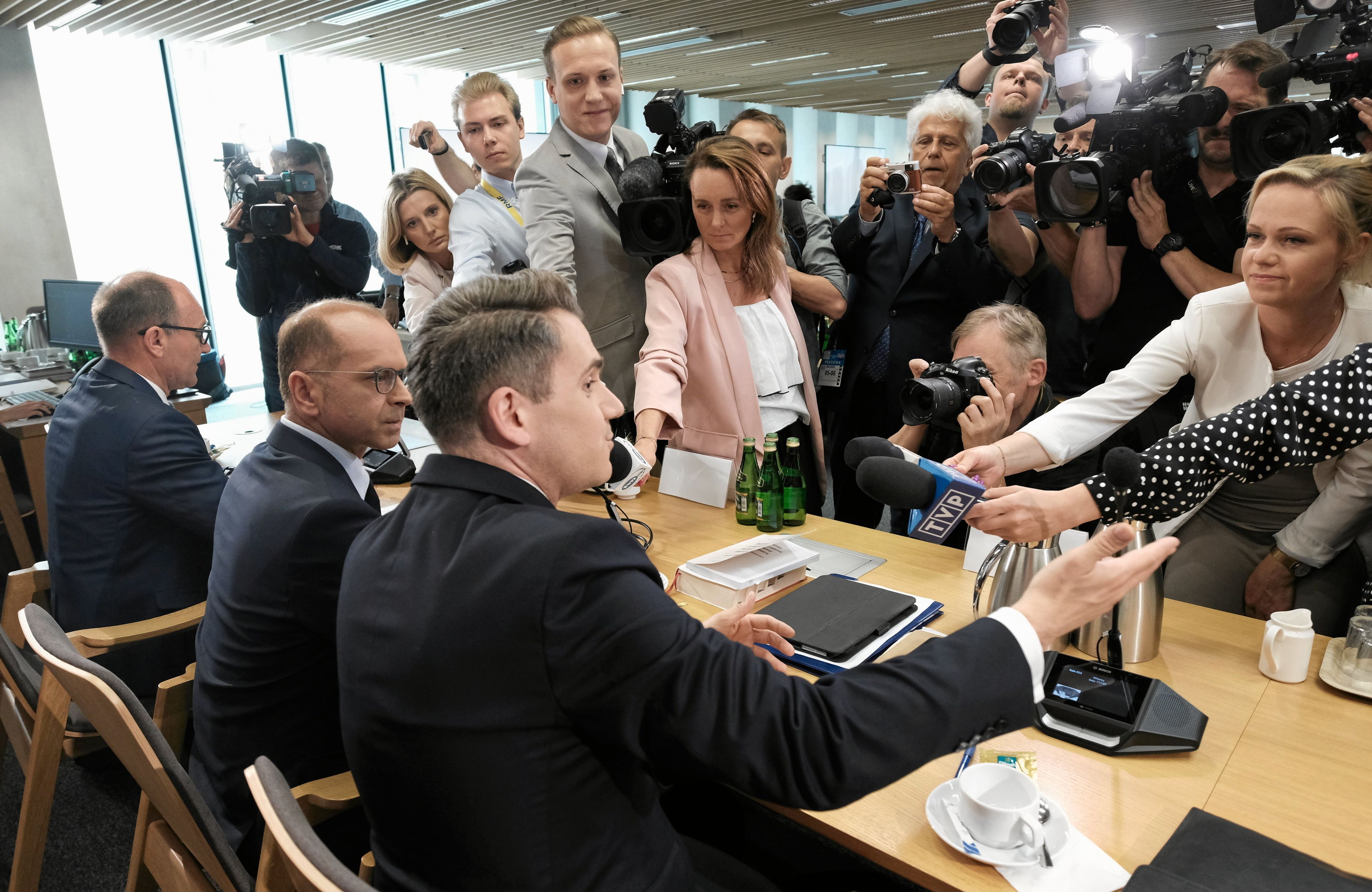 posłowie siedzą przy stole, przed nimi dziennikarze