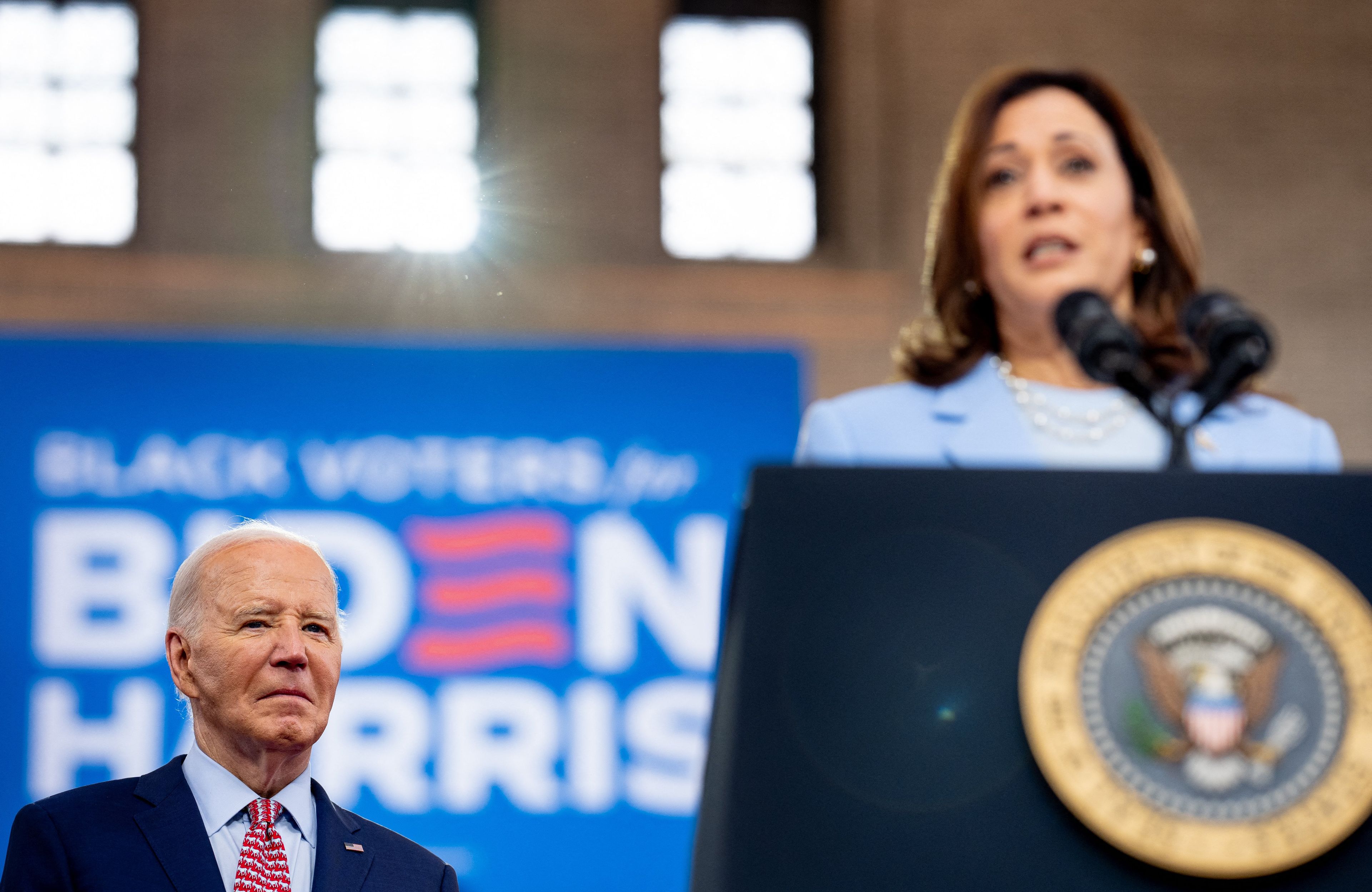 Na pierwszym planie Kamala Harris na mównicy, na drugim Joe Biden, na dnimi reflektory sceniczne