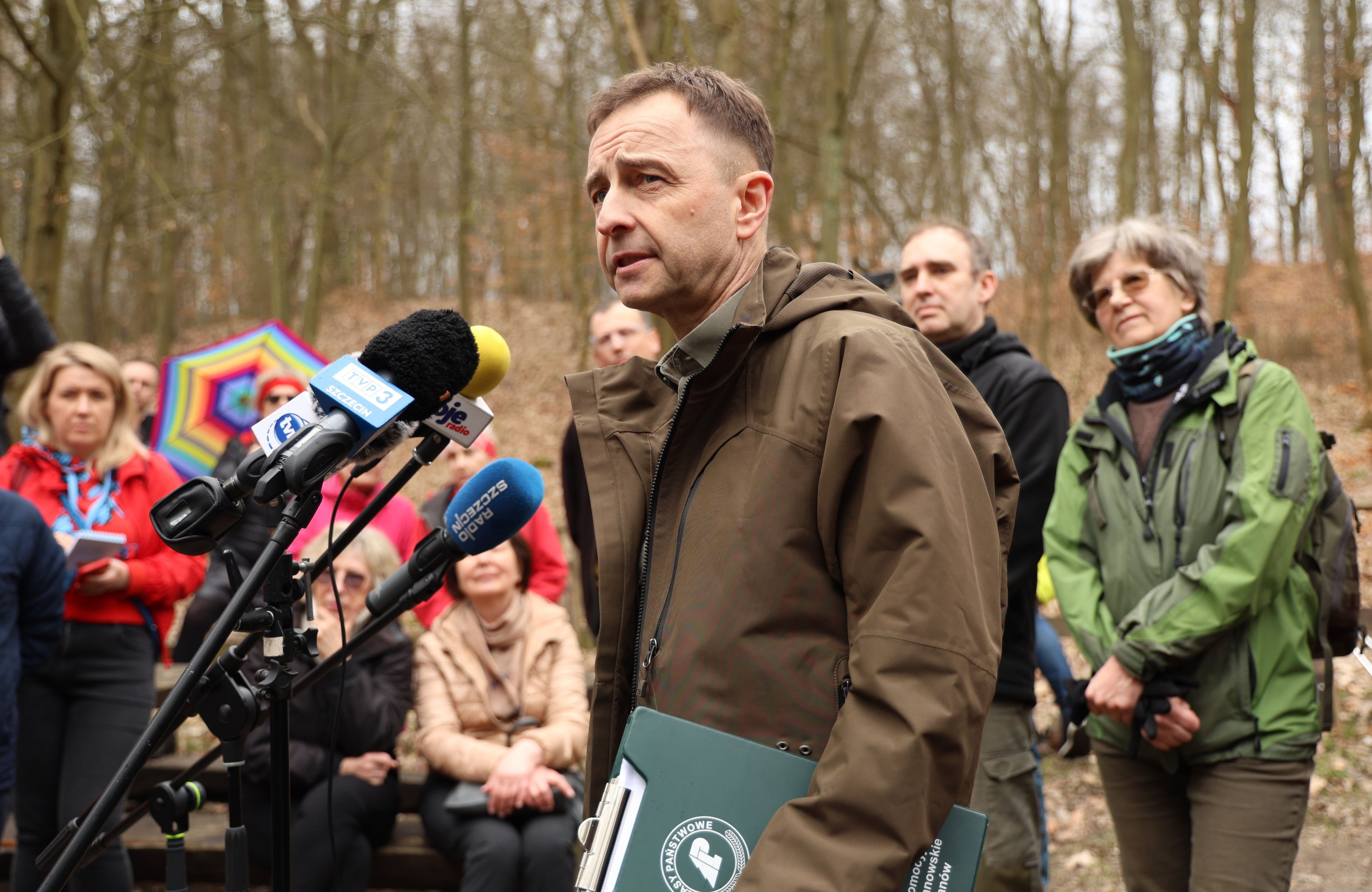 mężczyzna w brązowej kurtce wypowiada się do mikrofonu
