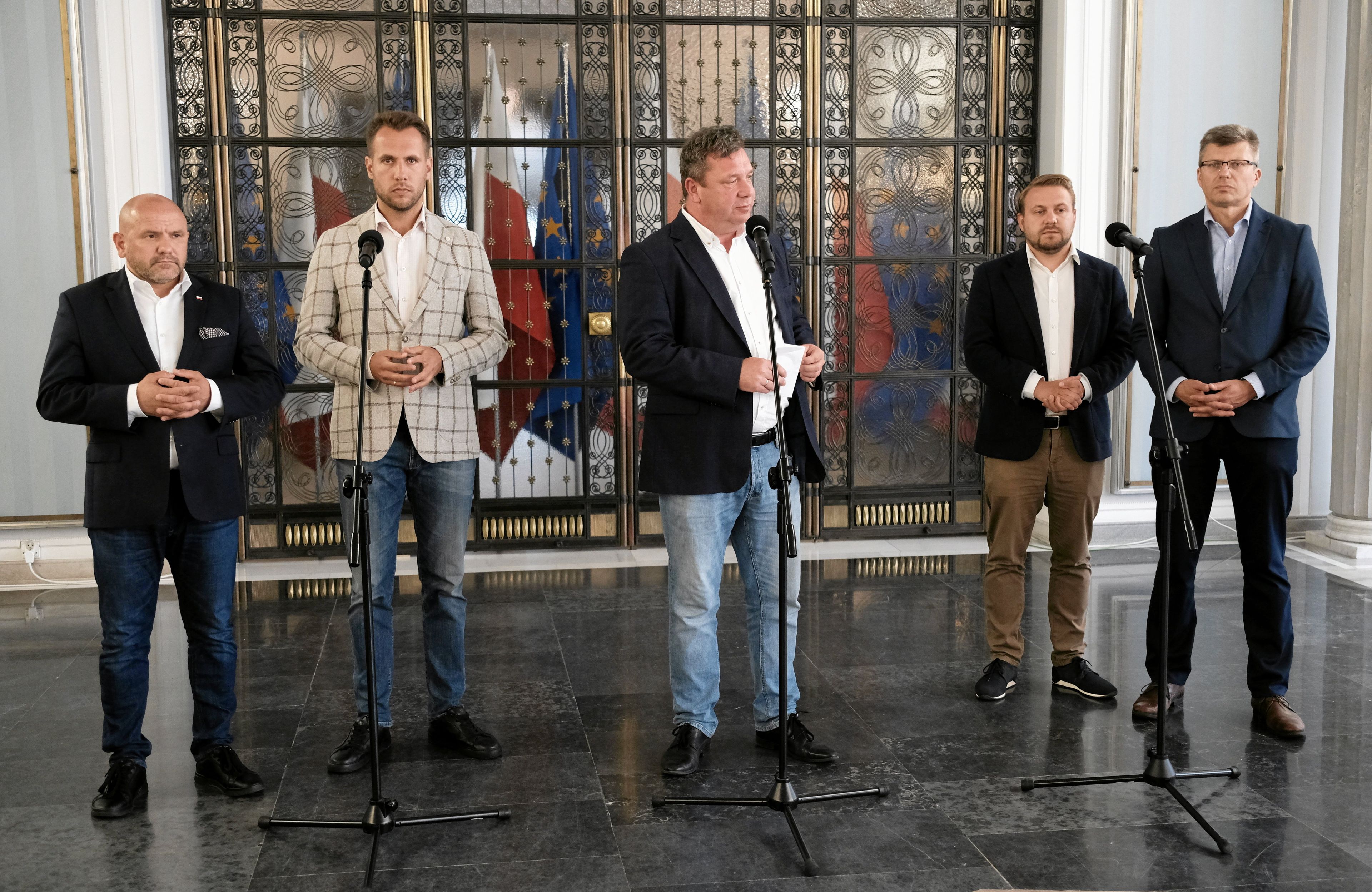 Politycy Suwerennej Polski stoją w rzędzie przed mikrofonami w Sali Kolumnowej Sejmu, ubrani są nieformalnie, w marynarki i dżinsy