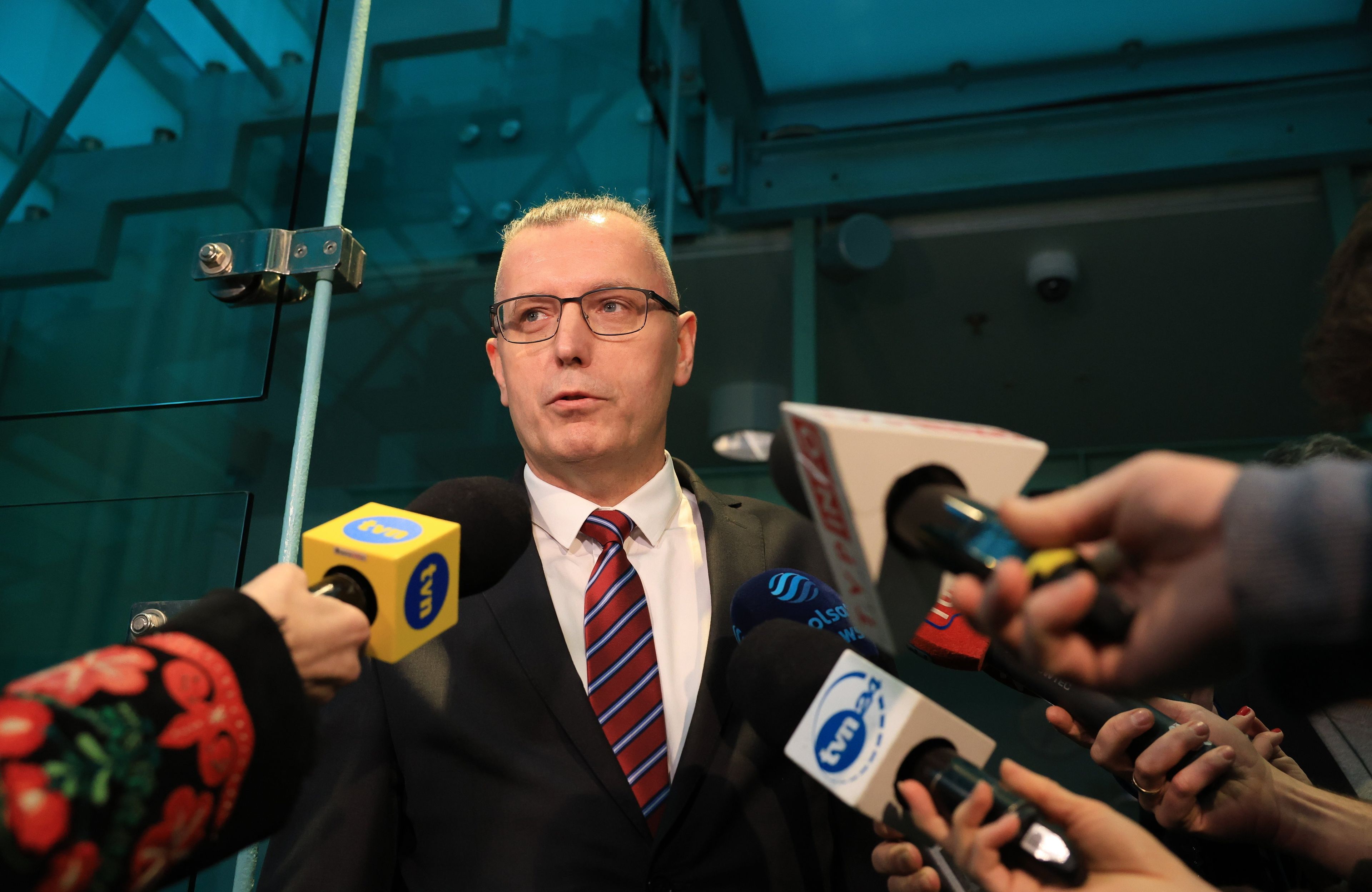 Mężczyzna w garniturze stoi przed mikrofonami mediów