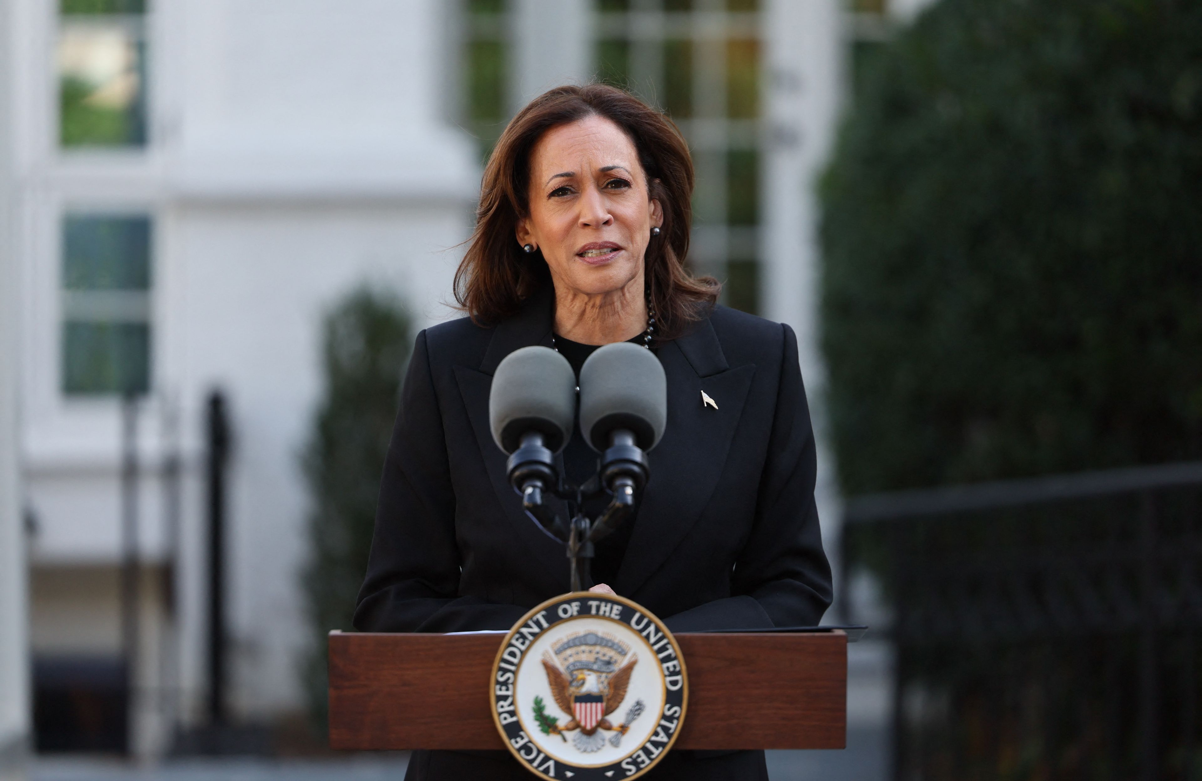 Kamala Harris w czarnym stroju przed dwoma mikrofonami i pulpitem na świeżym powietrzu