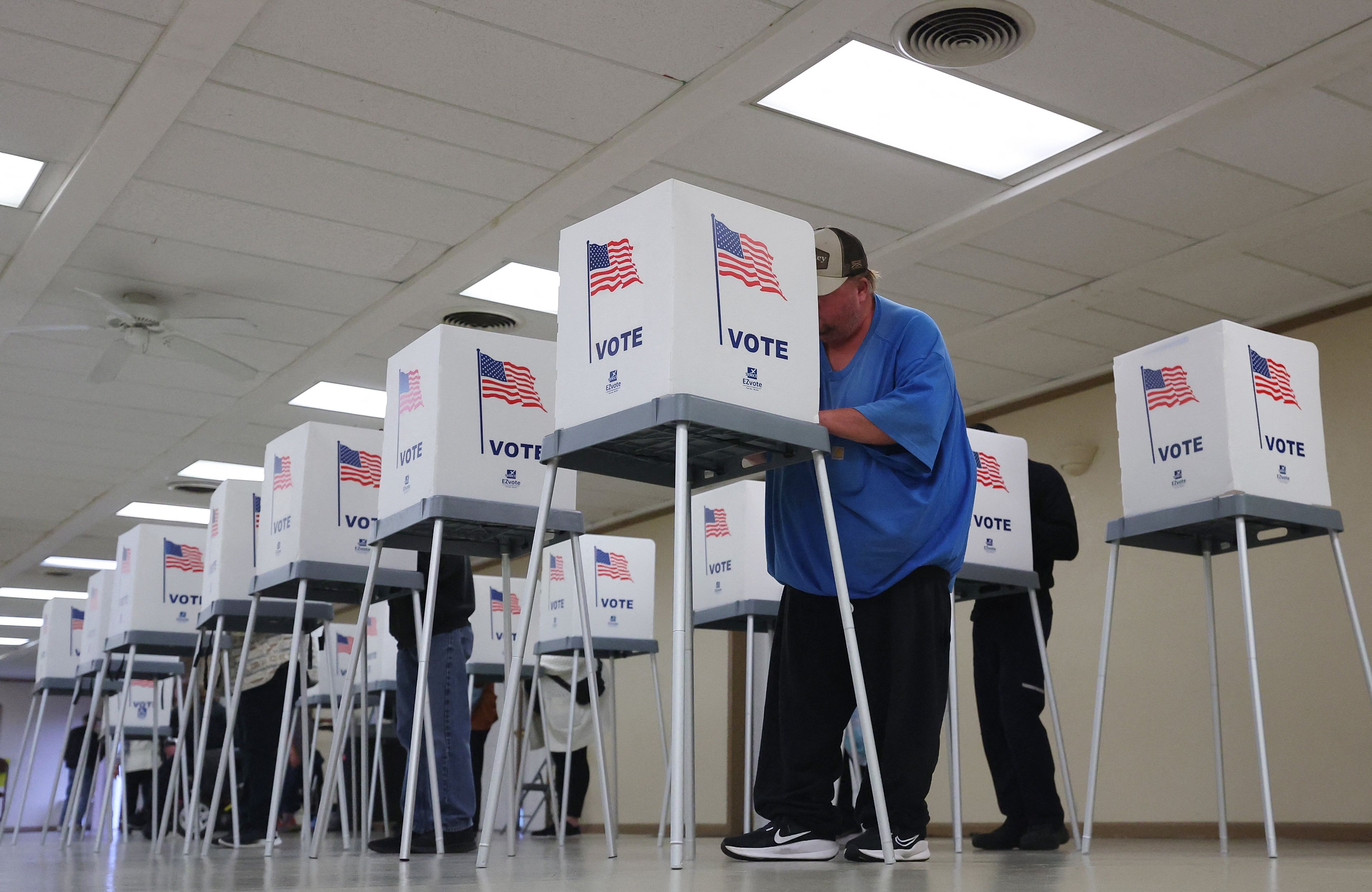 Mężczyzna głosuje w boksie z amerykańską flagą i napisem Vote