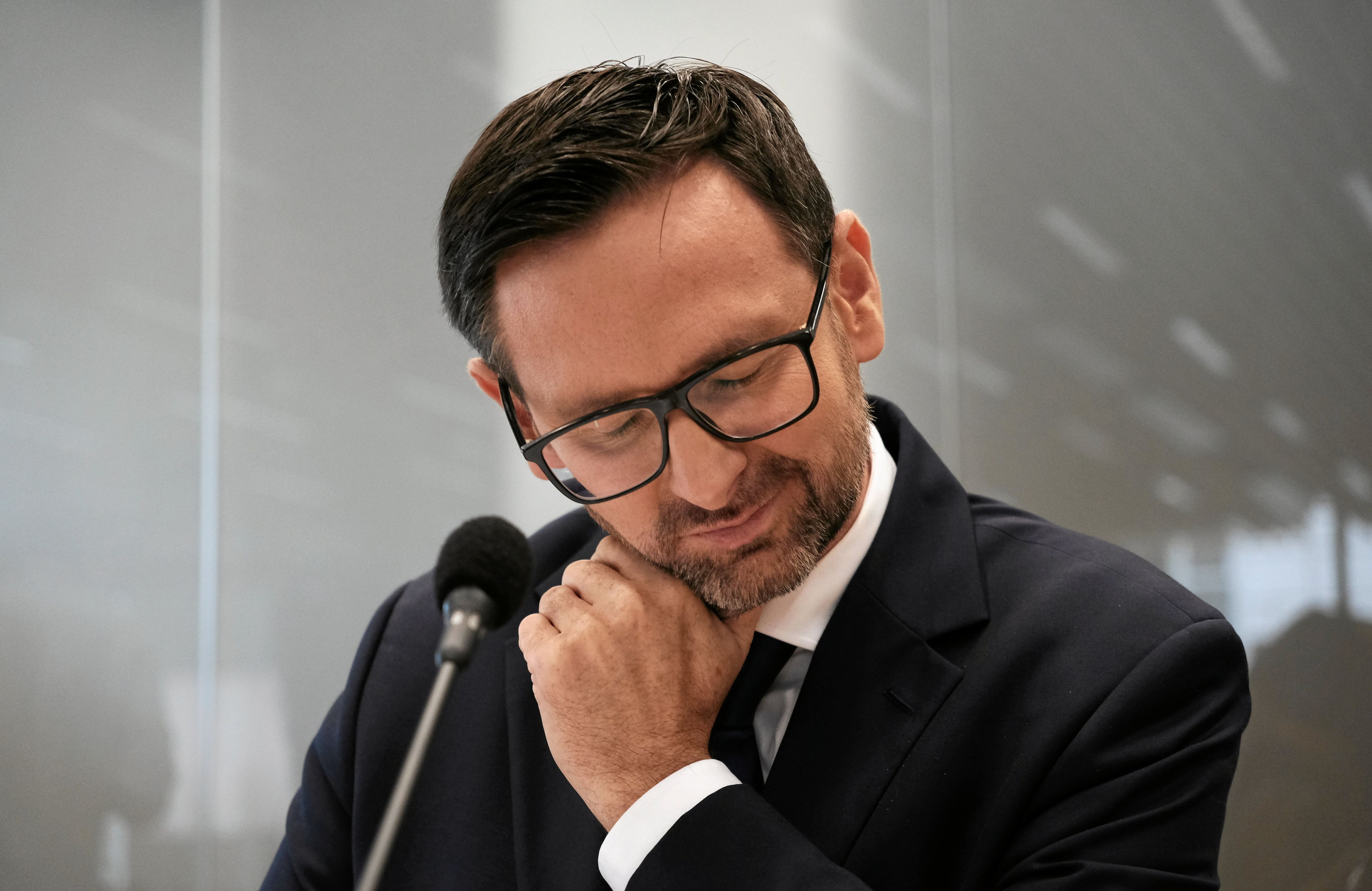 daniel obajtek mruży oczy siedząc przy mikrofonie podparty ręką - obrady komisji śledczej