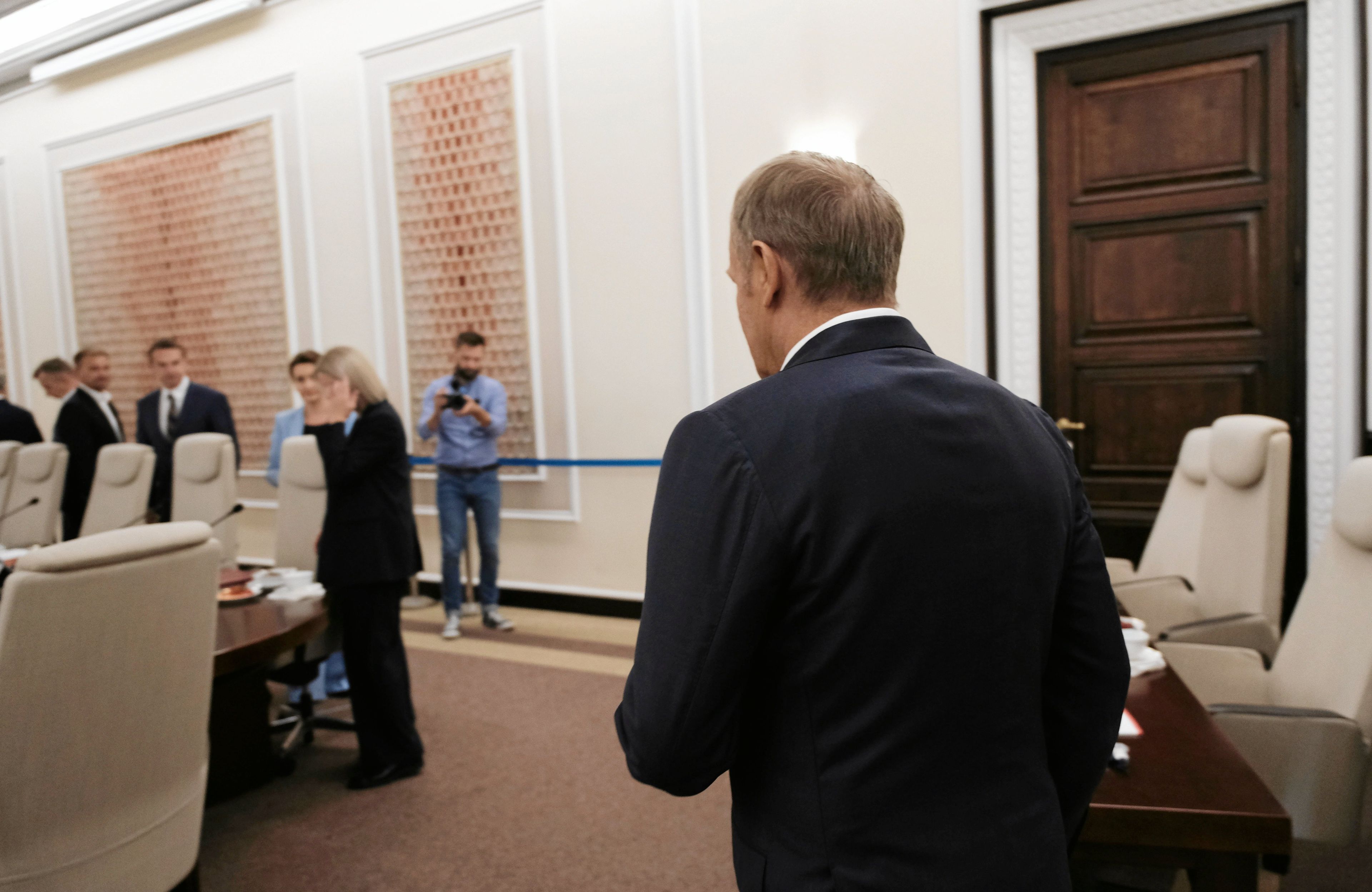 Donald Tusk wchodzi do sali na posiedzenie rządu, jest odwrócony plecami do obiektywu, w tle stoją ministrowie