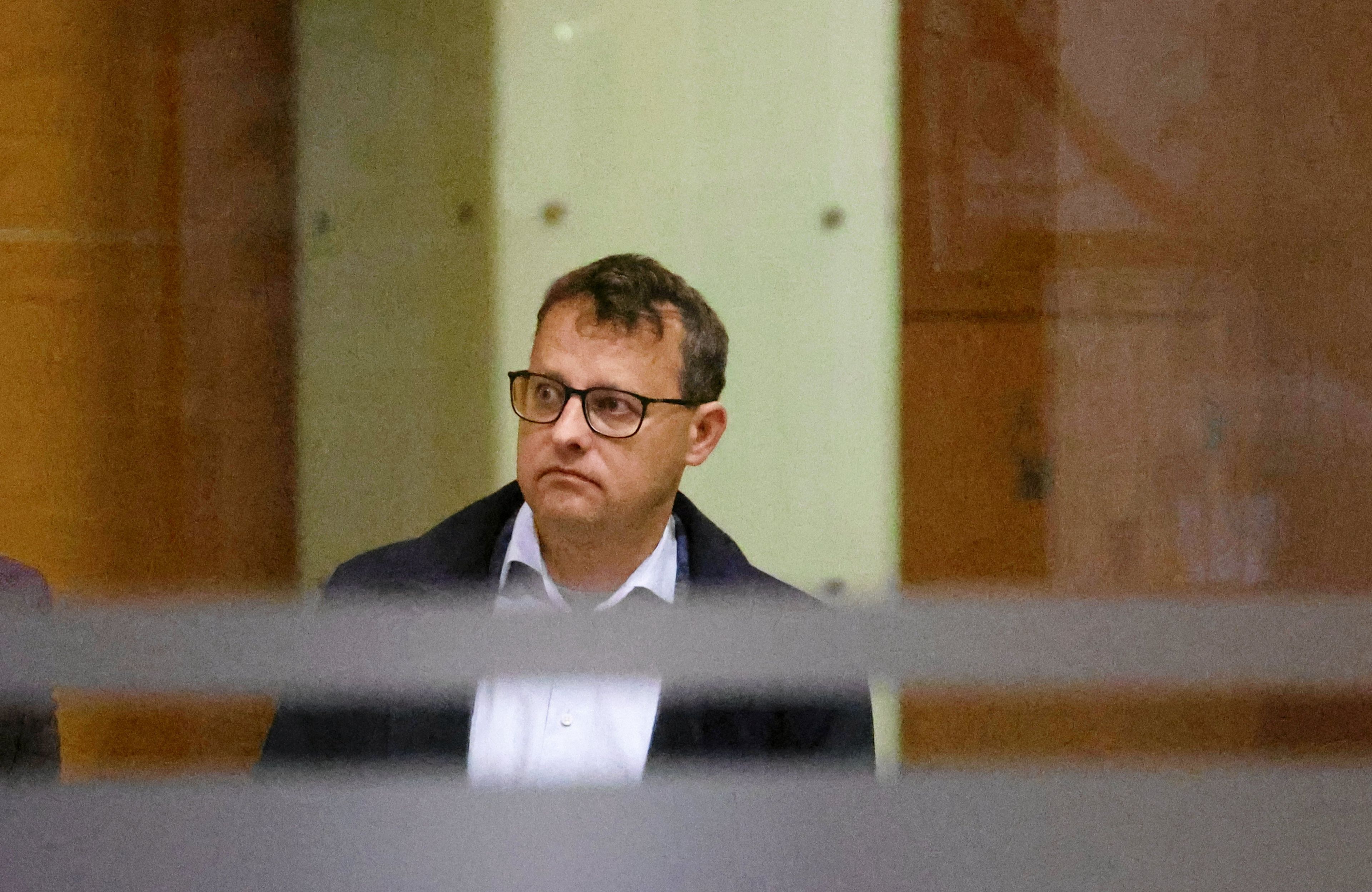 Mężczyzna w białej koszuli i płaszczu (Marcin Romanowski) sfotografowany przez szybę witryny