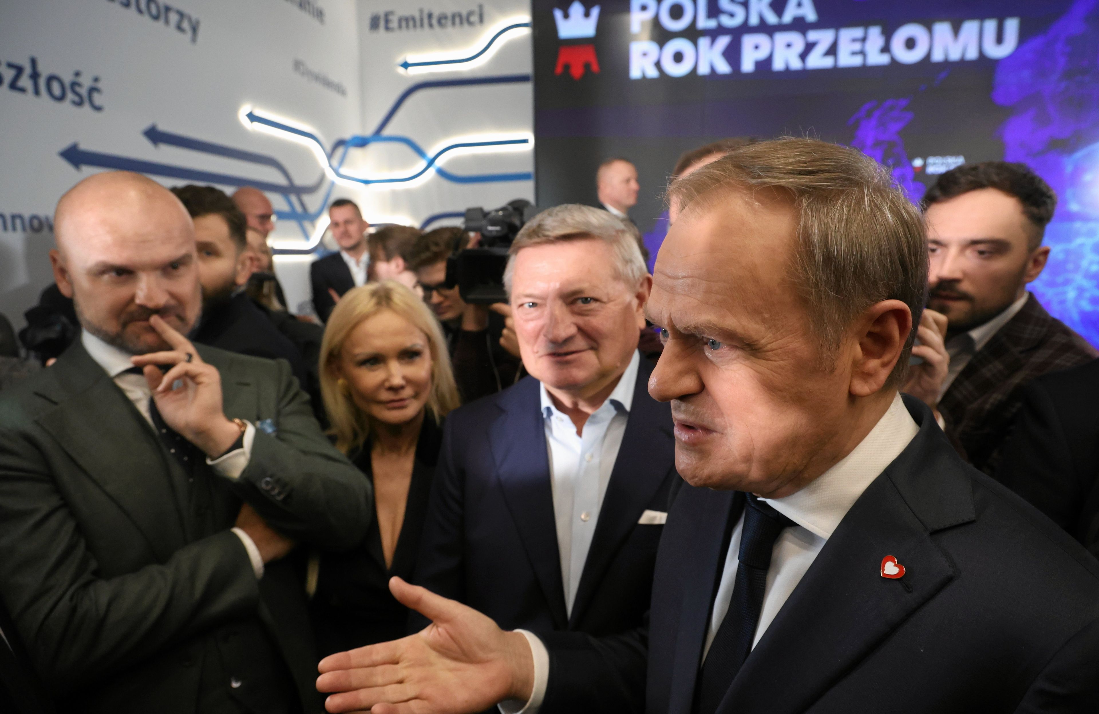 Kilku męzczyzn w garniturach, w tle napis na ścianie Rok przełomu