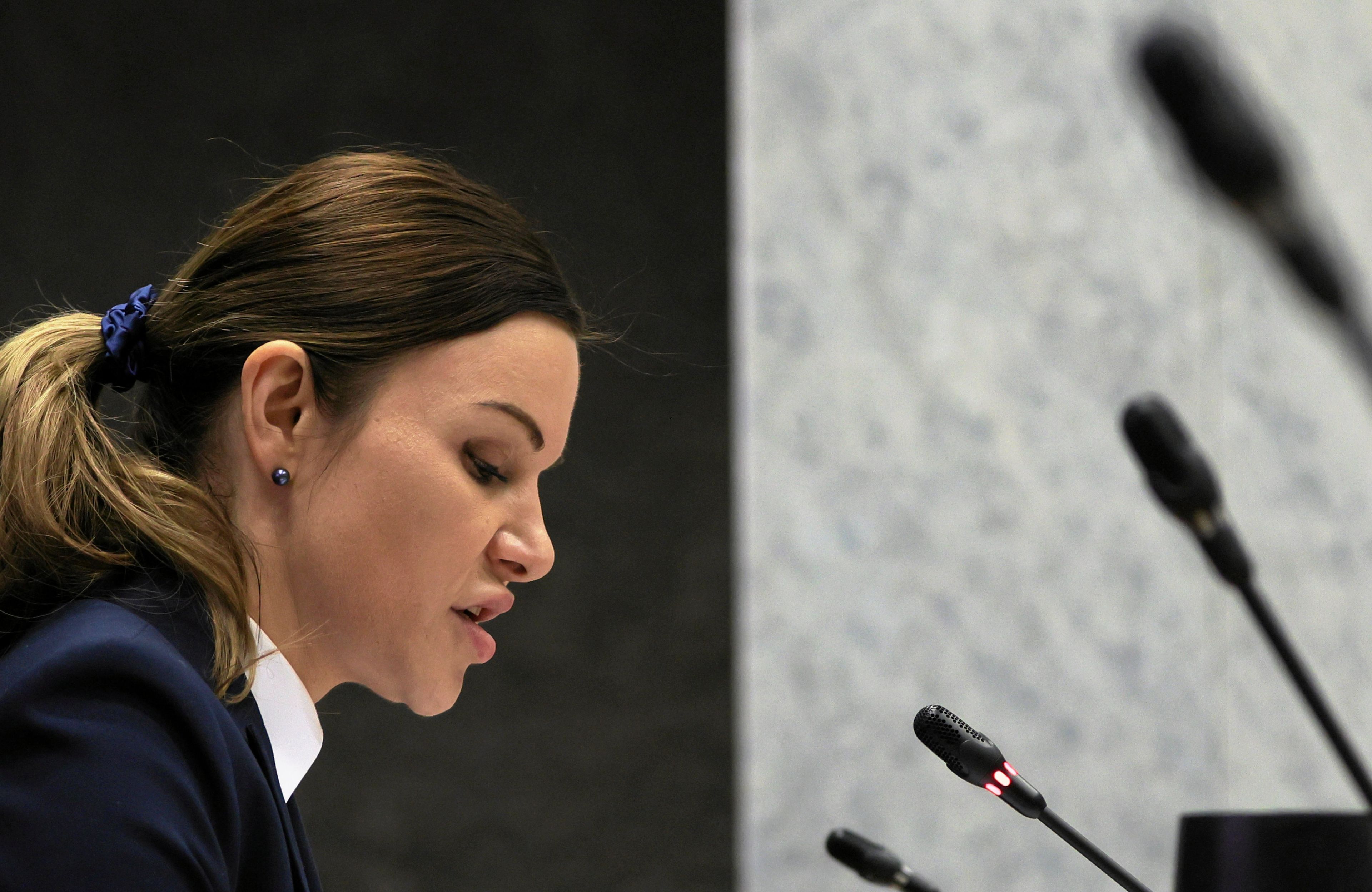 Na zdjęciu głowa kobiety z profilu. Kobieta ma przed sobą mikrofony.