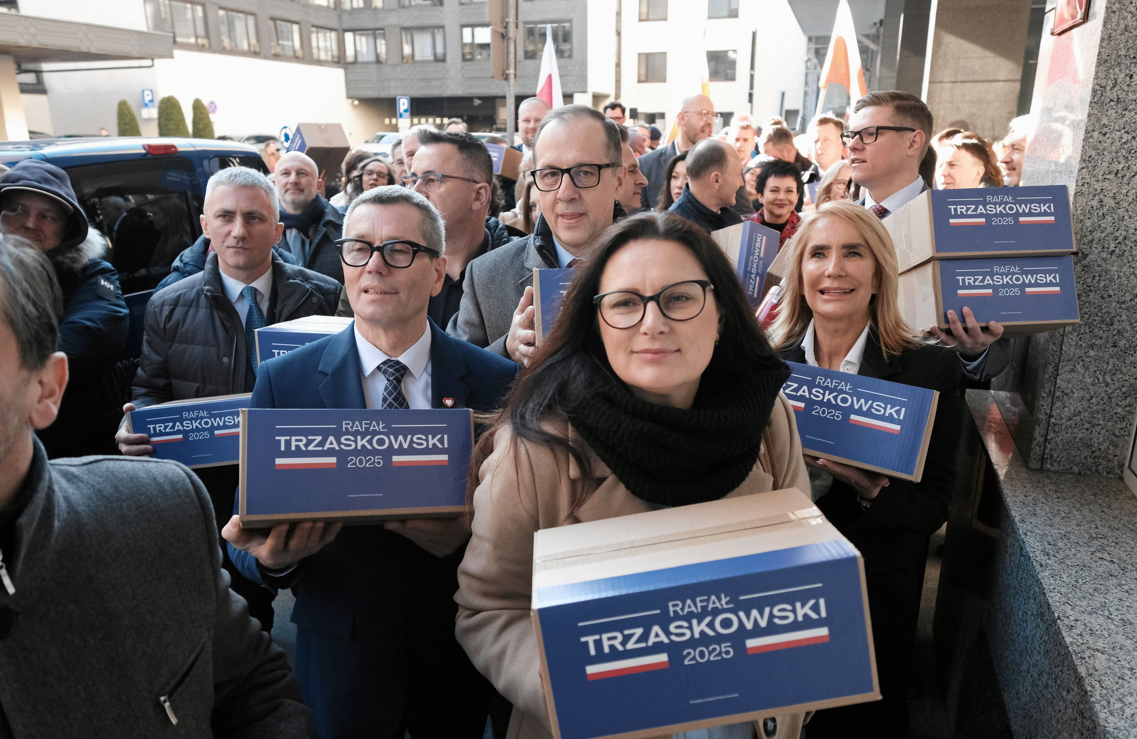 Ludzie niosą pudła opisane logiem kampanii wyborczej Rafała Trzaskowskiegi