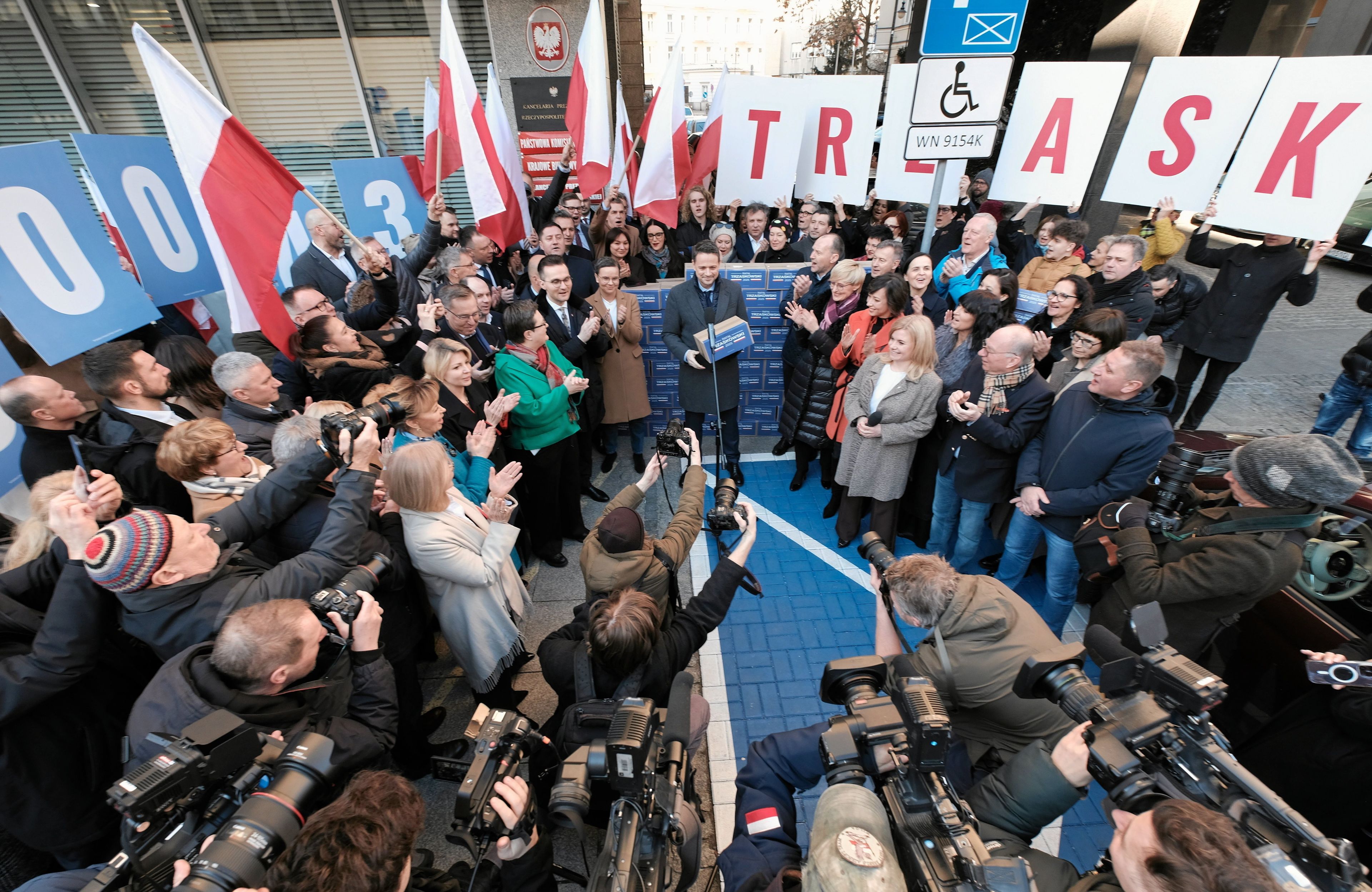 Tłum ludzi, wśród nich Rafał Trzaskowski z kartonem w ręku i ścianą kartonów obok