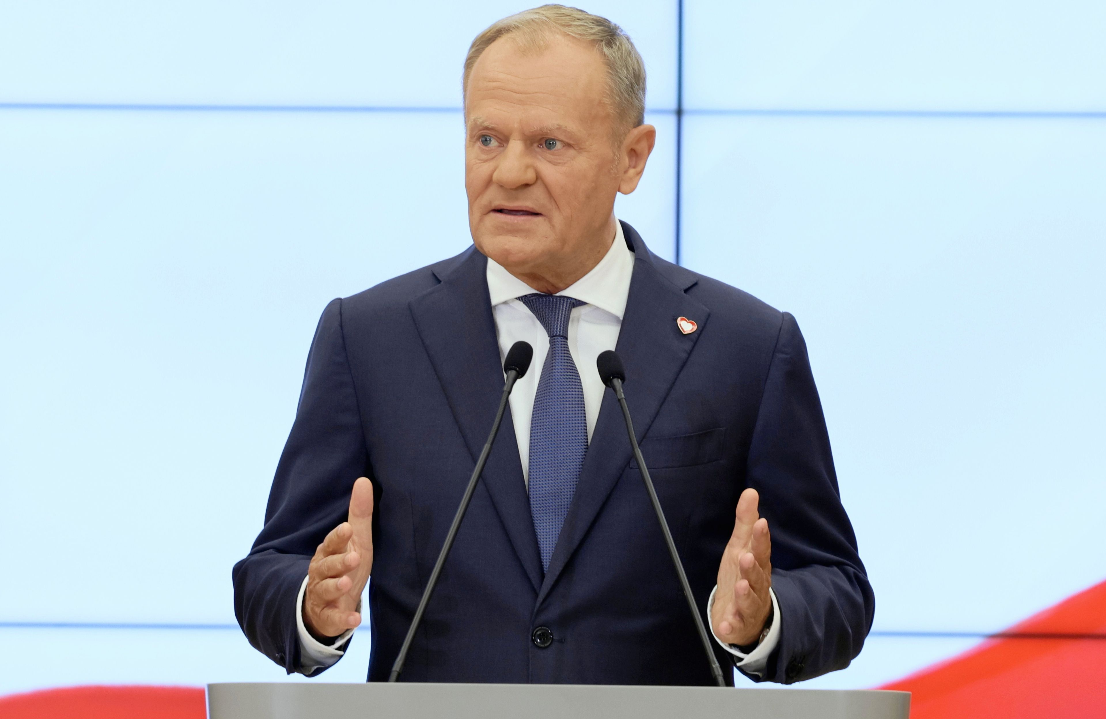 Mężczyzna w garniturze (Donald Tusk) gestykuluje przy mównicy