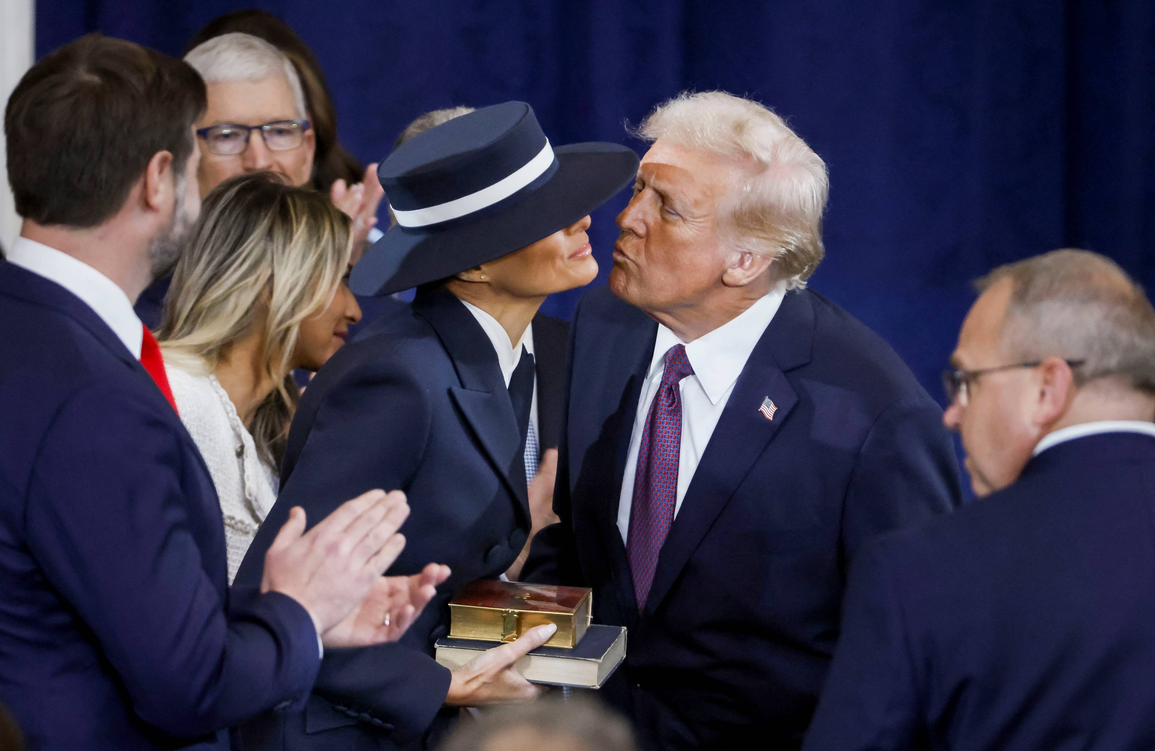 Donald Trump nachyla się, by pocałować żonę, wokół nich oficjele, żona Trumpa nosi bardzo duży kapelusz