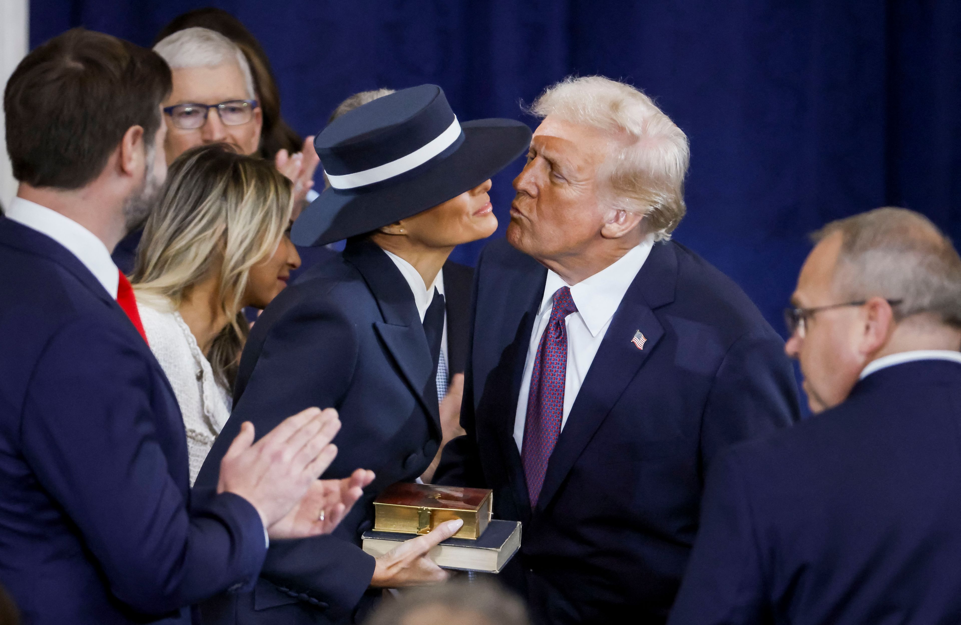 Donald Trump nachyla się, by pocałować żonę, wokół nich oficjele, żona Trumpa nosi bardzo duży kapelusz