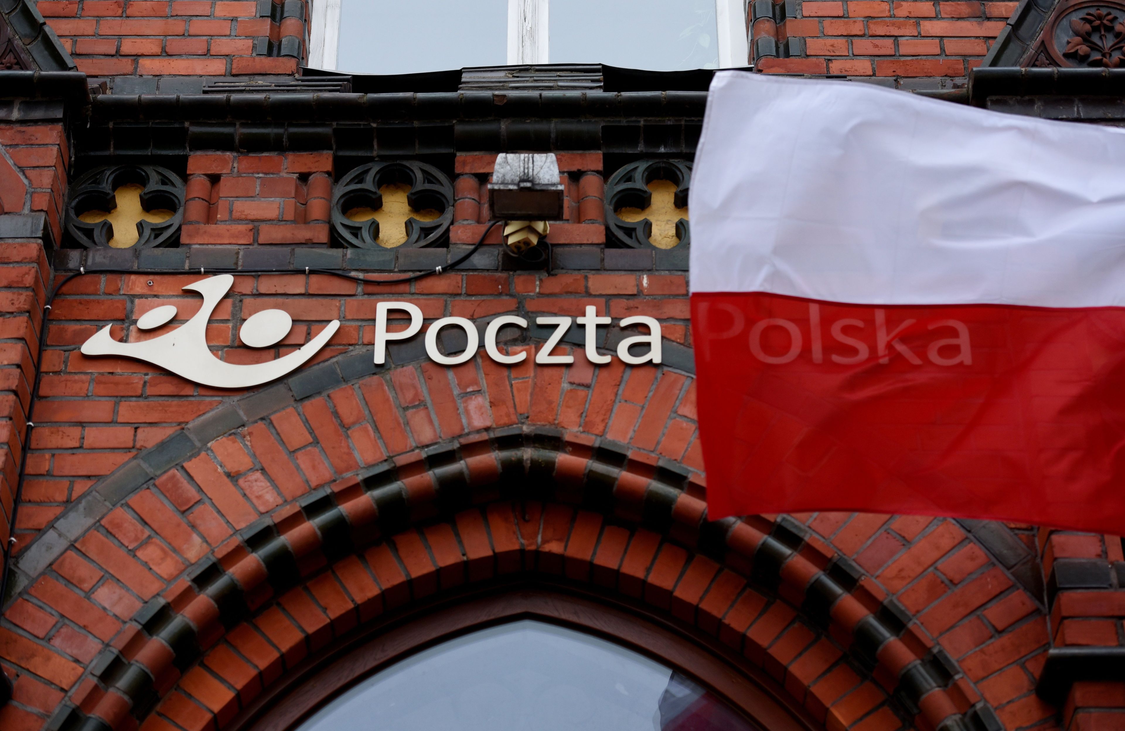 Ceglany budynek poczty, logo i napis poczta, powiewająca biało-czerwona flaga