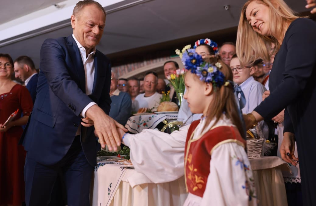 Mężczyzna w garniturze podaje dłoń dziewczynce w kolorowym stroju kaszubskim z wiankiem na głowie