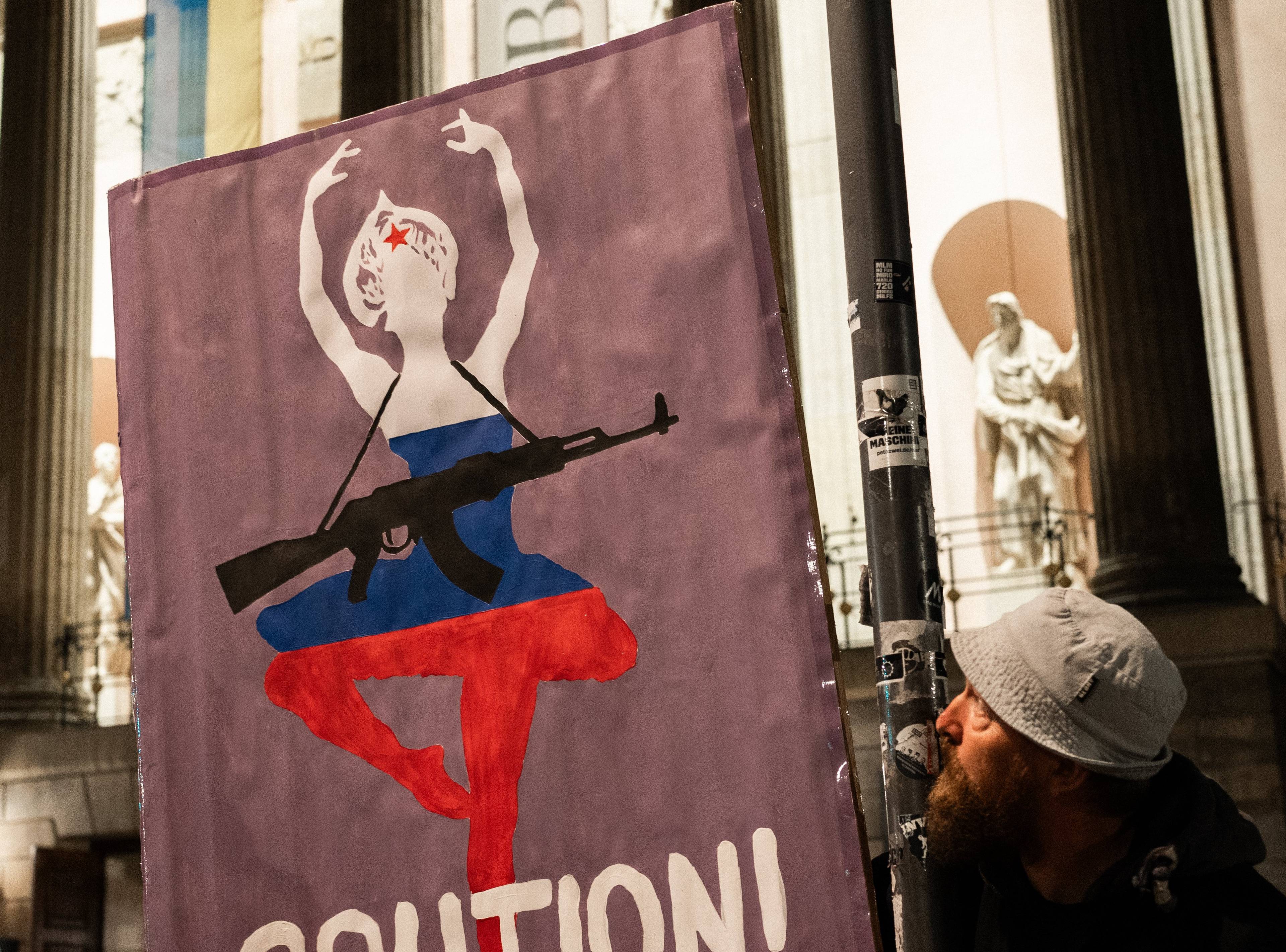 plakat trzymany przez demonstrantów z tancerką z kałasznikowem