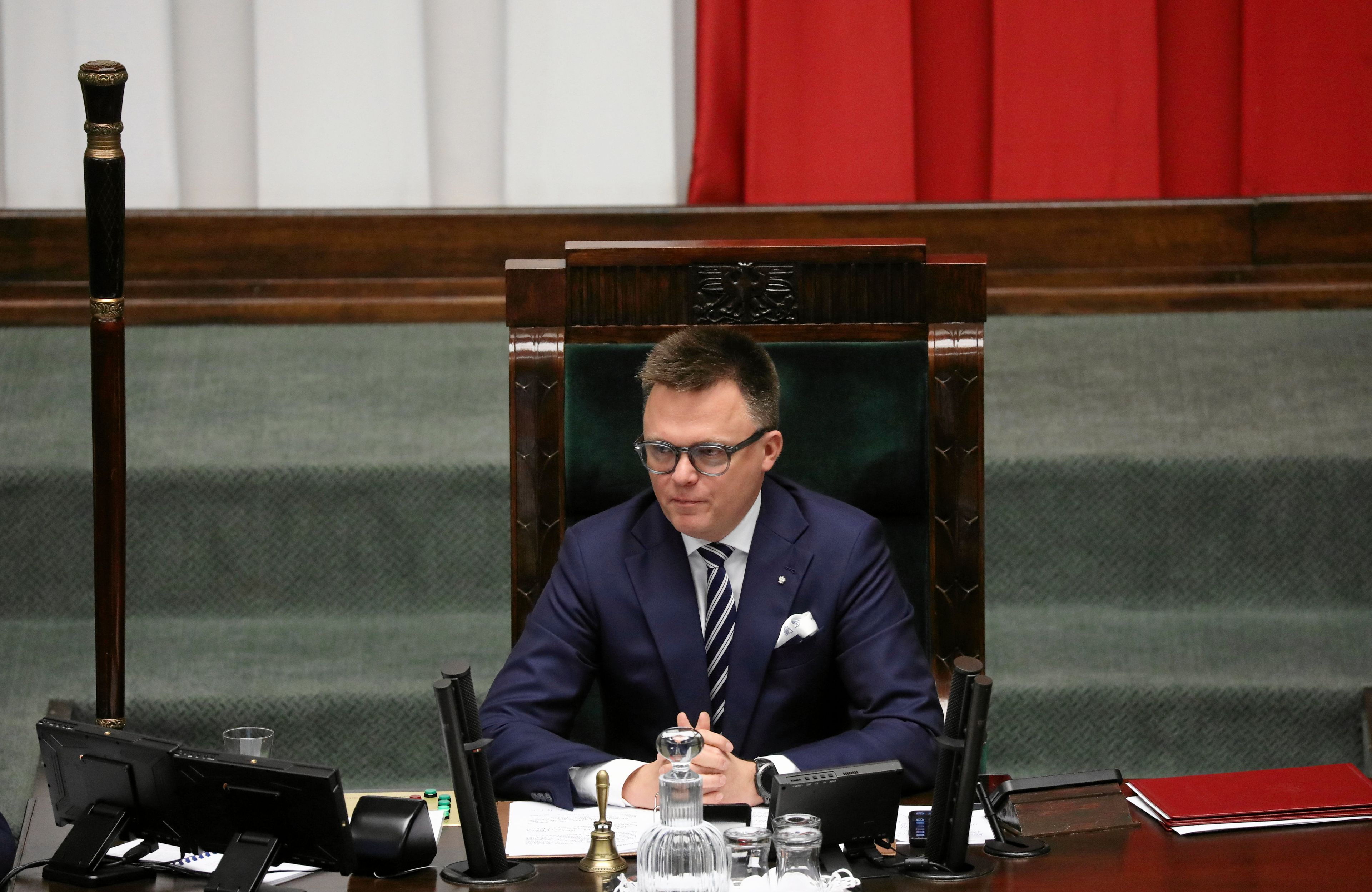 Mężczyzna w okularach siedzący w wysokim drewnianym fotelu za pulpitem