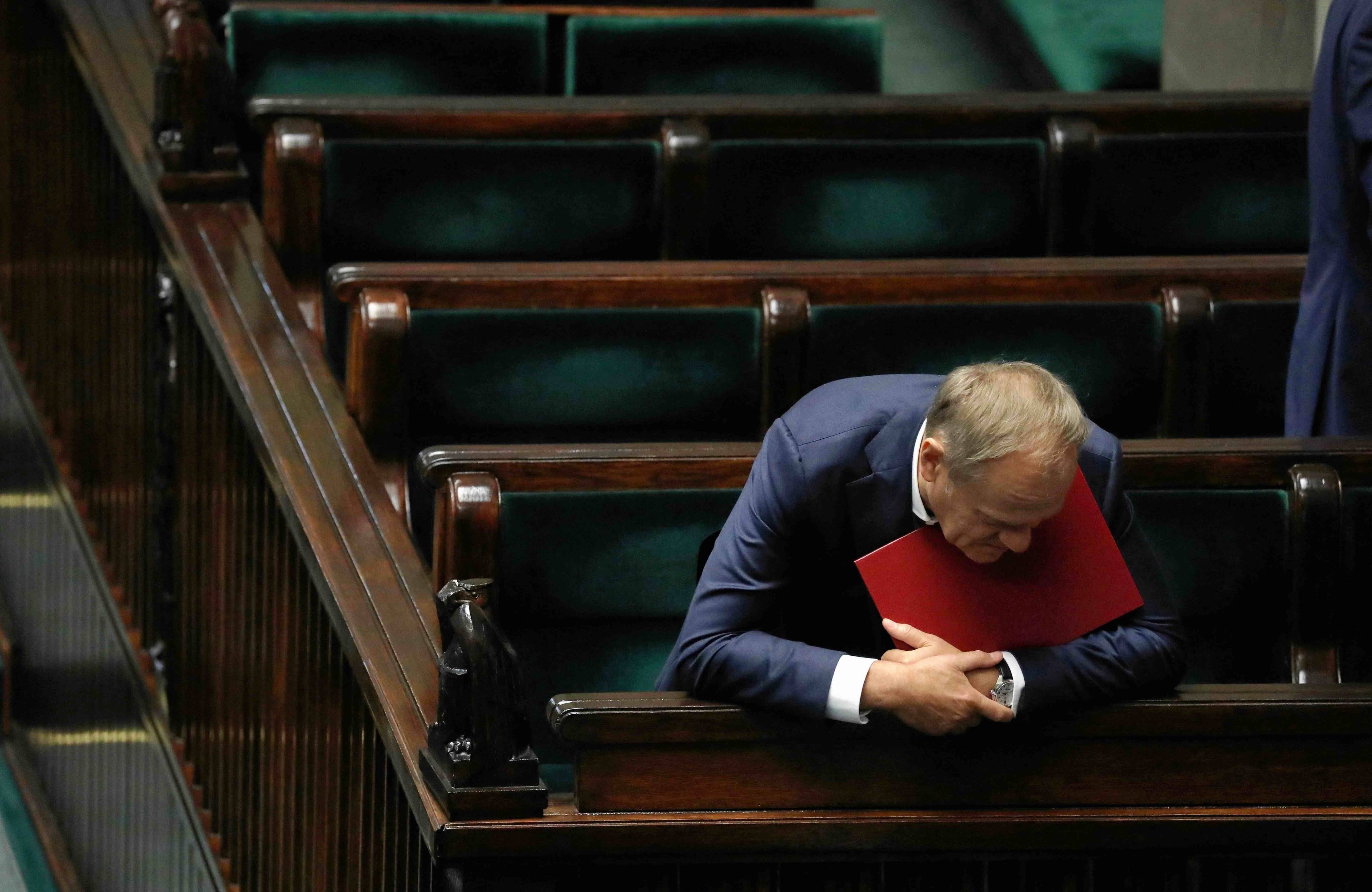 Donald Tusk wychyla się z ław rządowych w Sejmie, trzymając pod brodą czerwoną teczkę. Ustawa dekryminalizacyjna