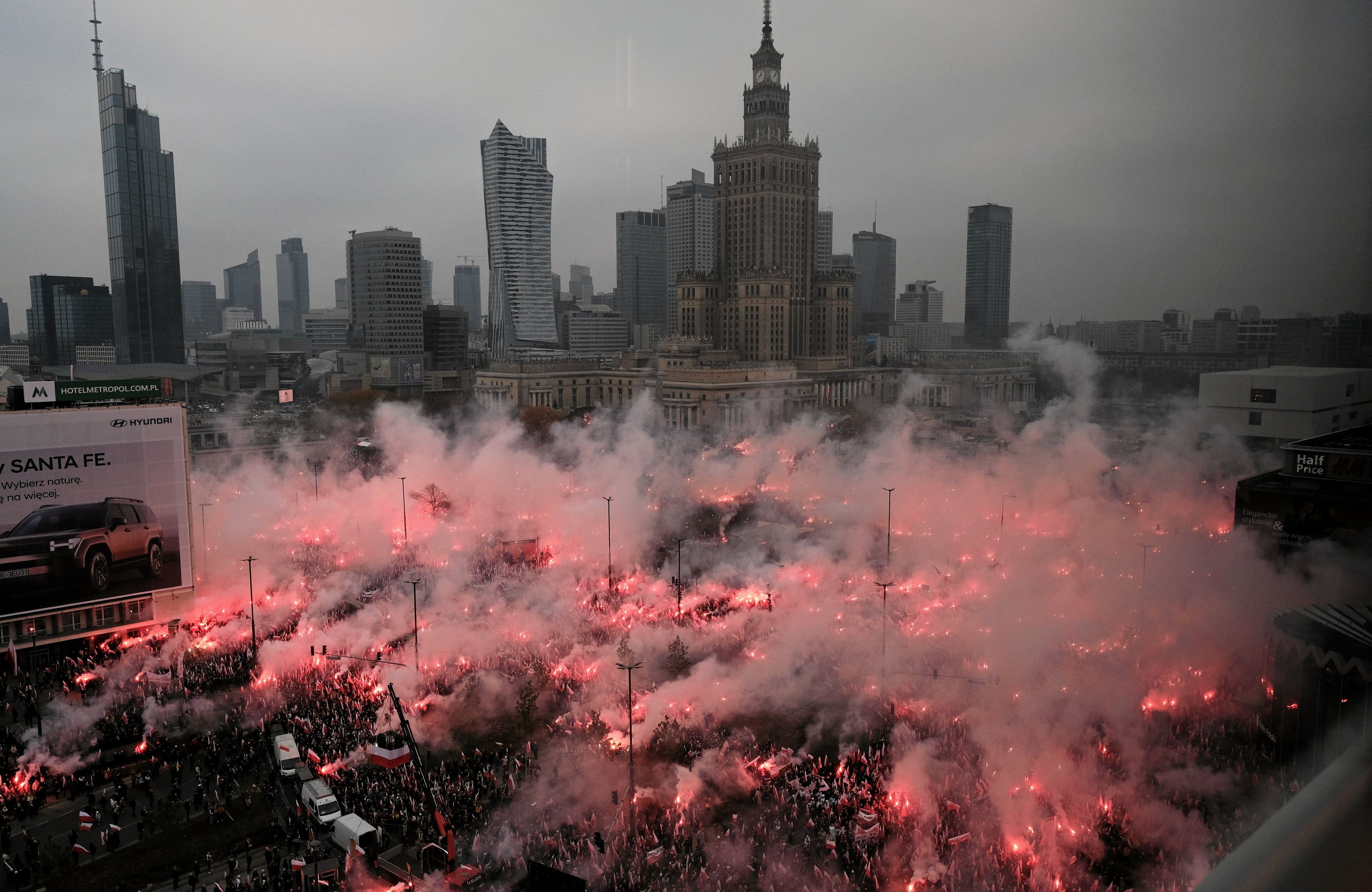 Marsz Niepodległości: widok na panoramę wieżowców w Warszawie i dym z rac w tłumie