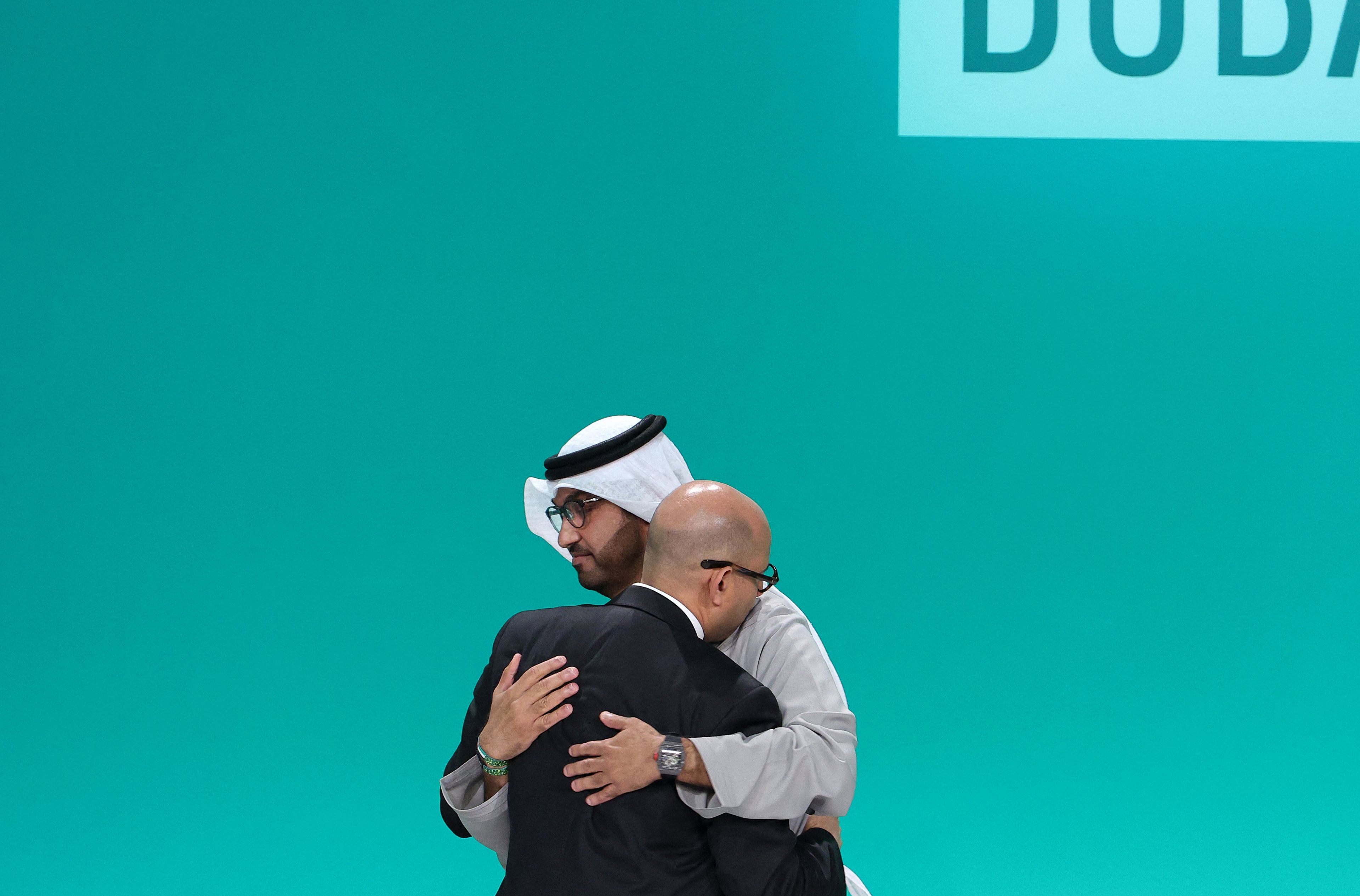 Prezydent COP28 Sultan Ahmed Al-Dżaber i sekretarz wykonawczy Ramowej konwencji Narodów Zjednoczonych w sprawie zmian klimatu (UNFCCC) Simon Stiell obejmują się na scenie podczas sesji plenarnej w trakcie szczytu klimatycznego ONZ w Dubaju. W tle napis Dubai
