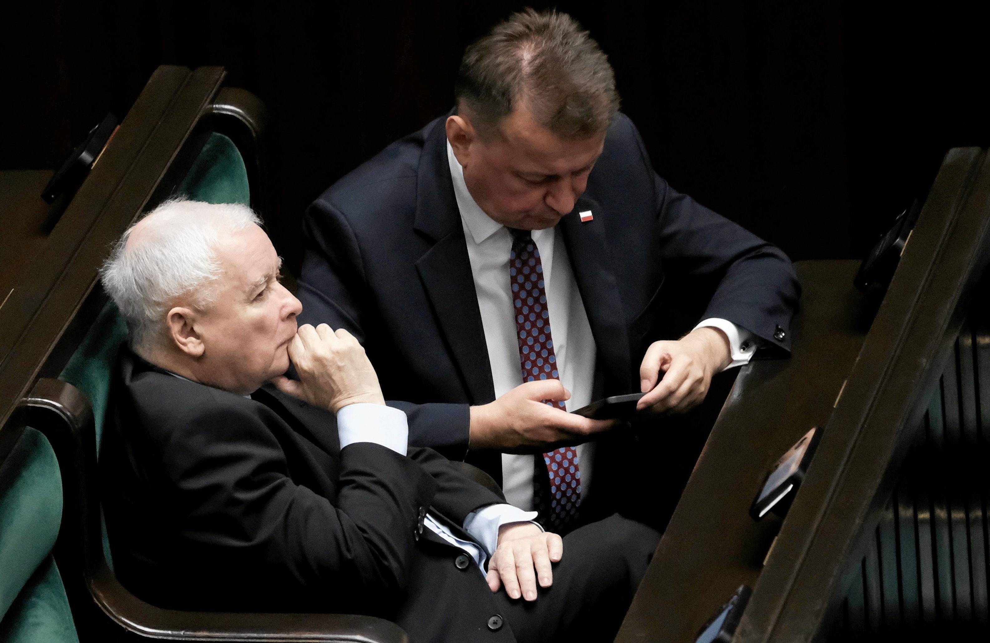 Jarosław Kaczyński siedzi w ławach poselskich w Sejmie, obok Marius Błaszczak patrzy w ekran telefonu.