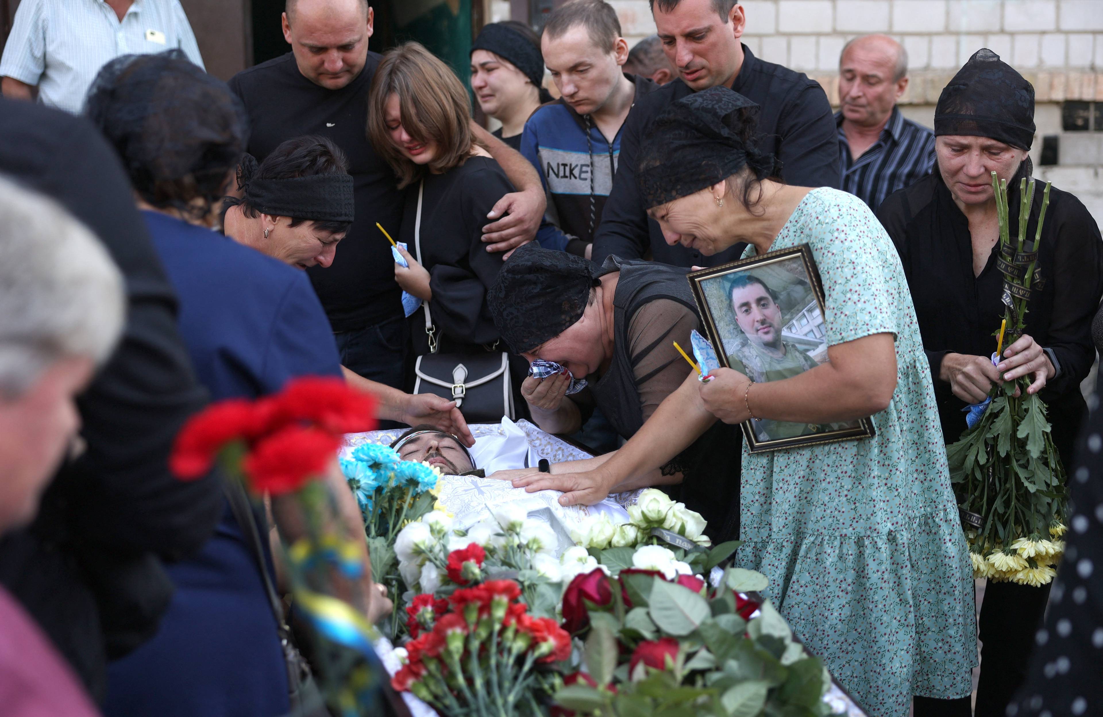 Rodzina żegna poległego żołnierza, ludzie płaczą nad trumną, przy niej widać kwiaty