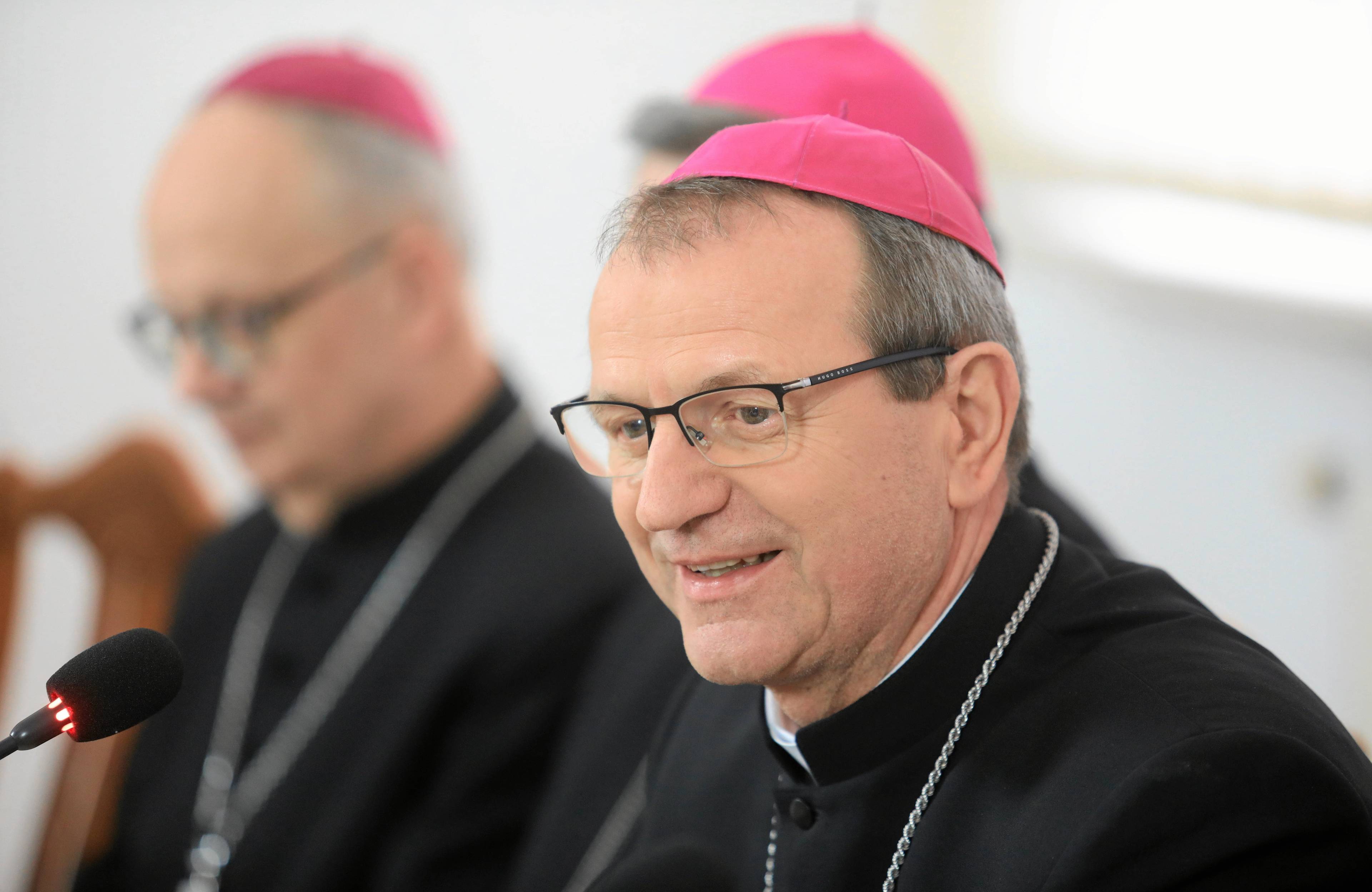 Mężczyzna, ksiądz, w okularach, siedzi, ma strój biskupi