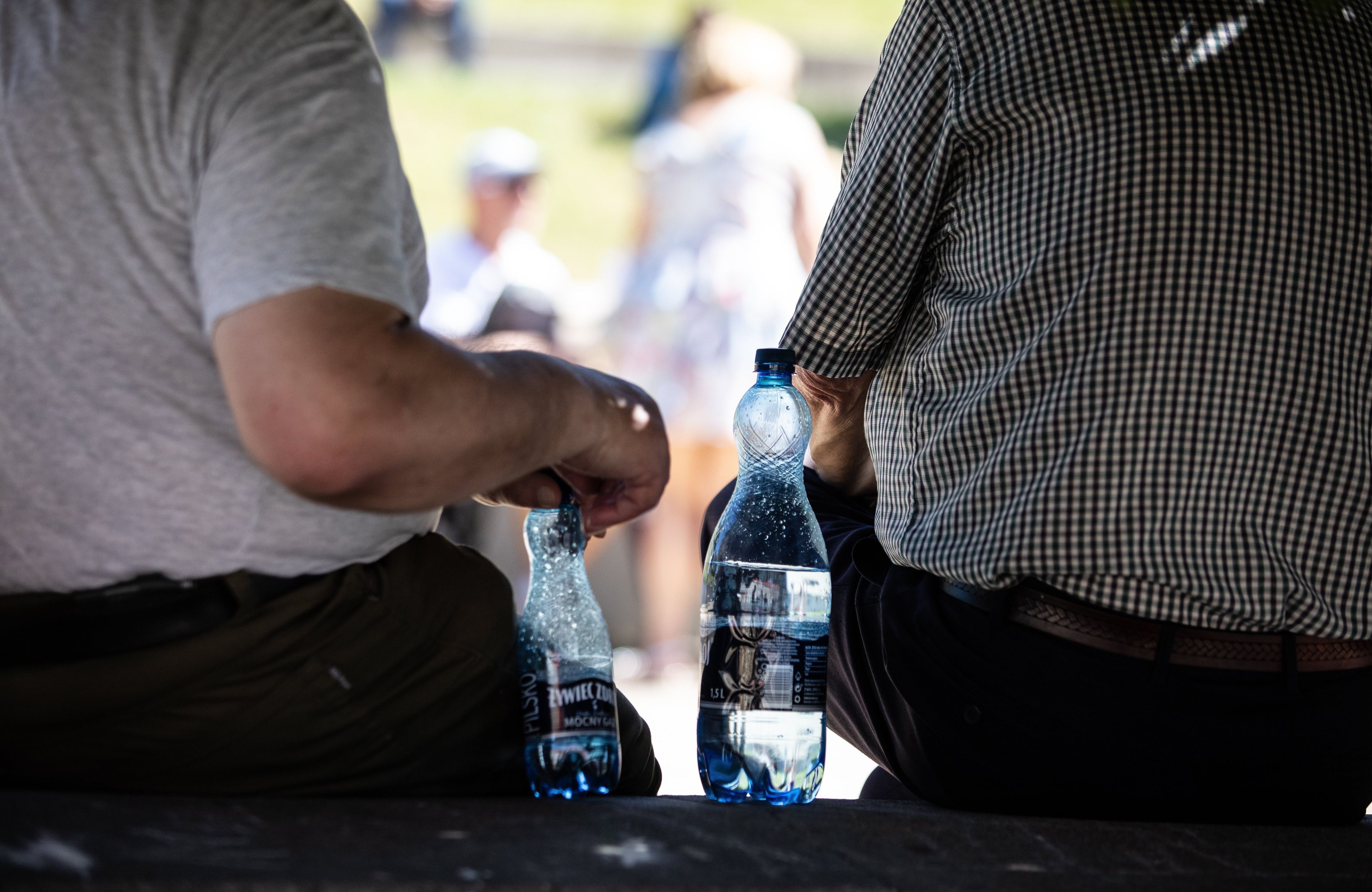Dwaj mężczyźni, tyłem, na ławce między nimi dwie plastikowe butelki wody