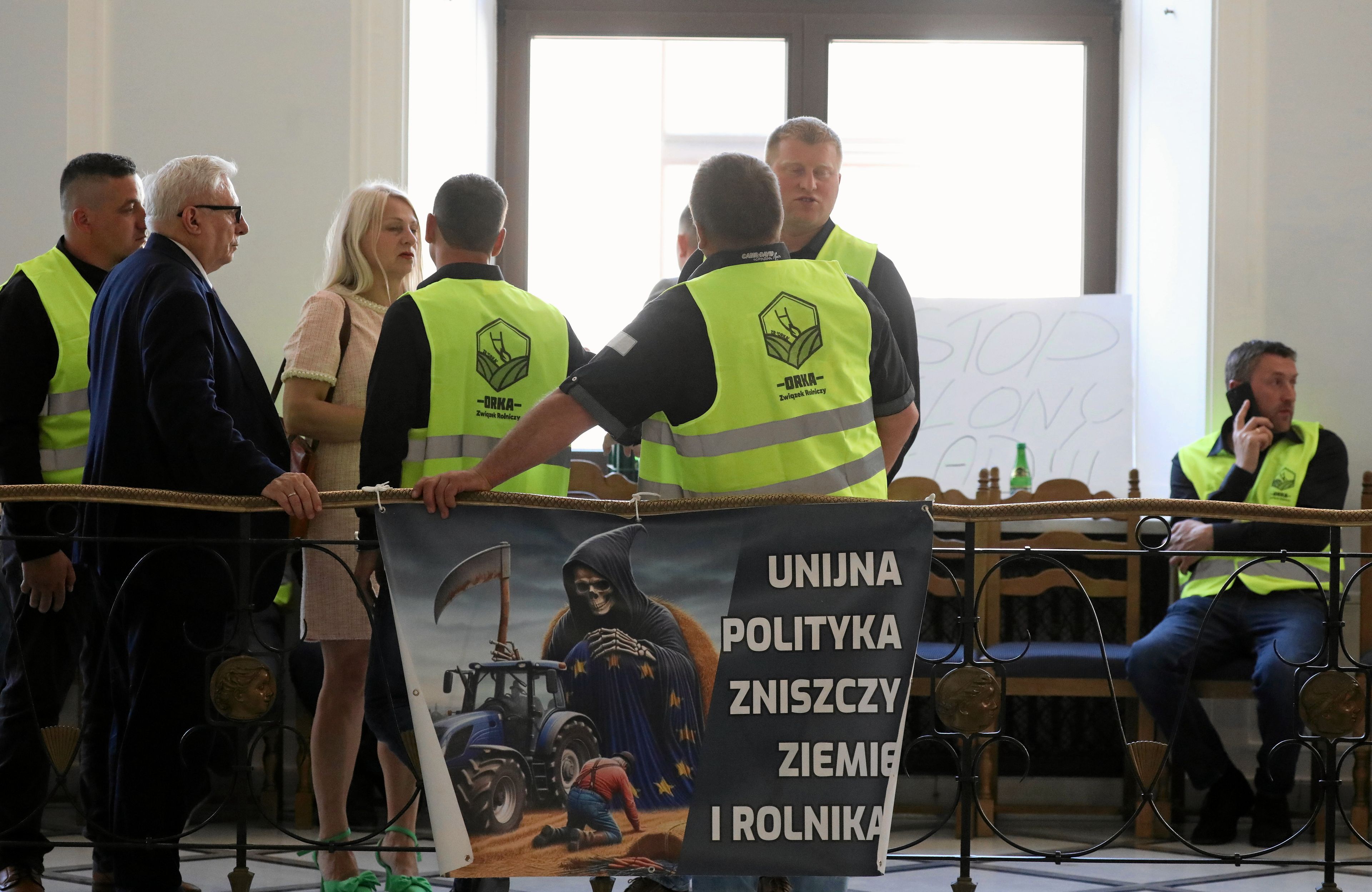 Na zdjęciu widzimy koryatrze sejmowe. Na nich mężczyźni w żółtych kamizelkach protestacyjnych z logo roganizacji rolniczej "Orka". Mężczyźni rozmawiają z posłami PiS