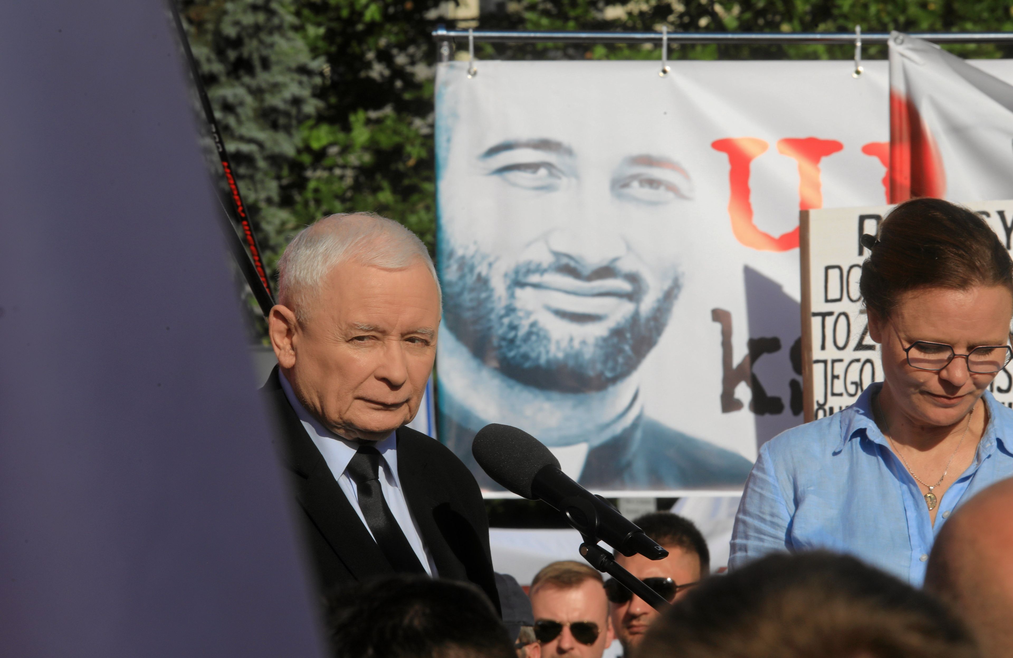 kaczyński na tle plakatu z księdzem o