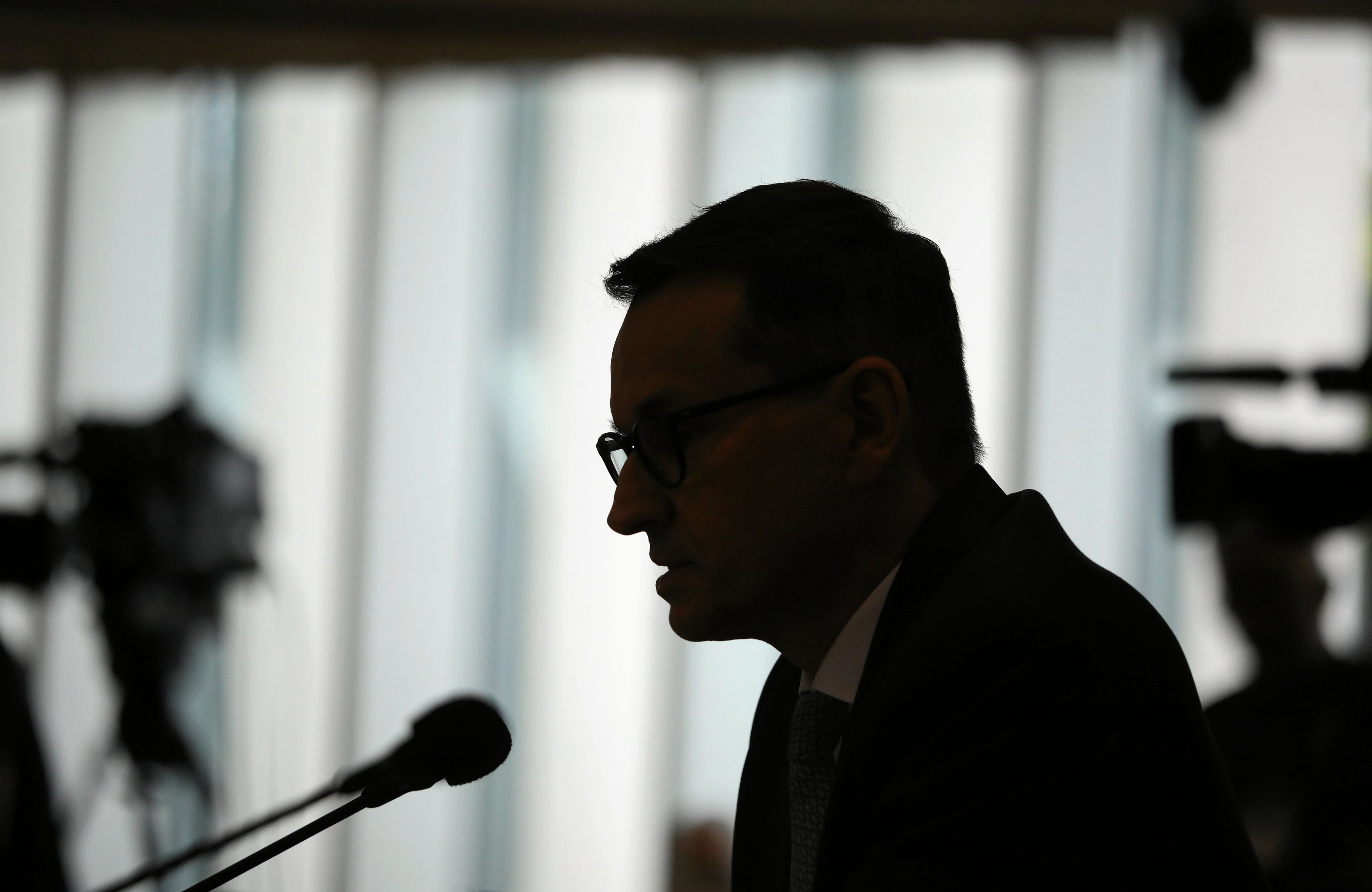 ciemny profil przemawiającego do mikrofonu mężczyzny w okularach