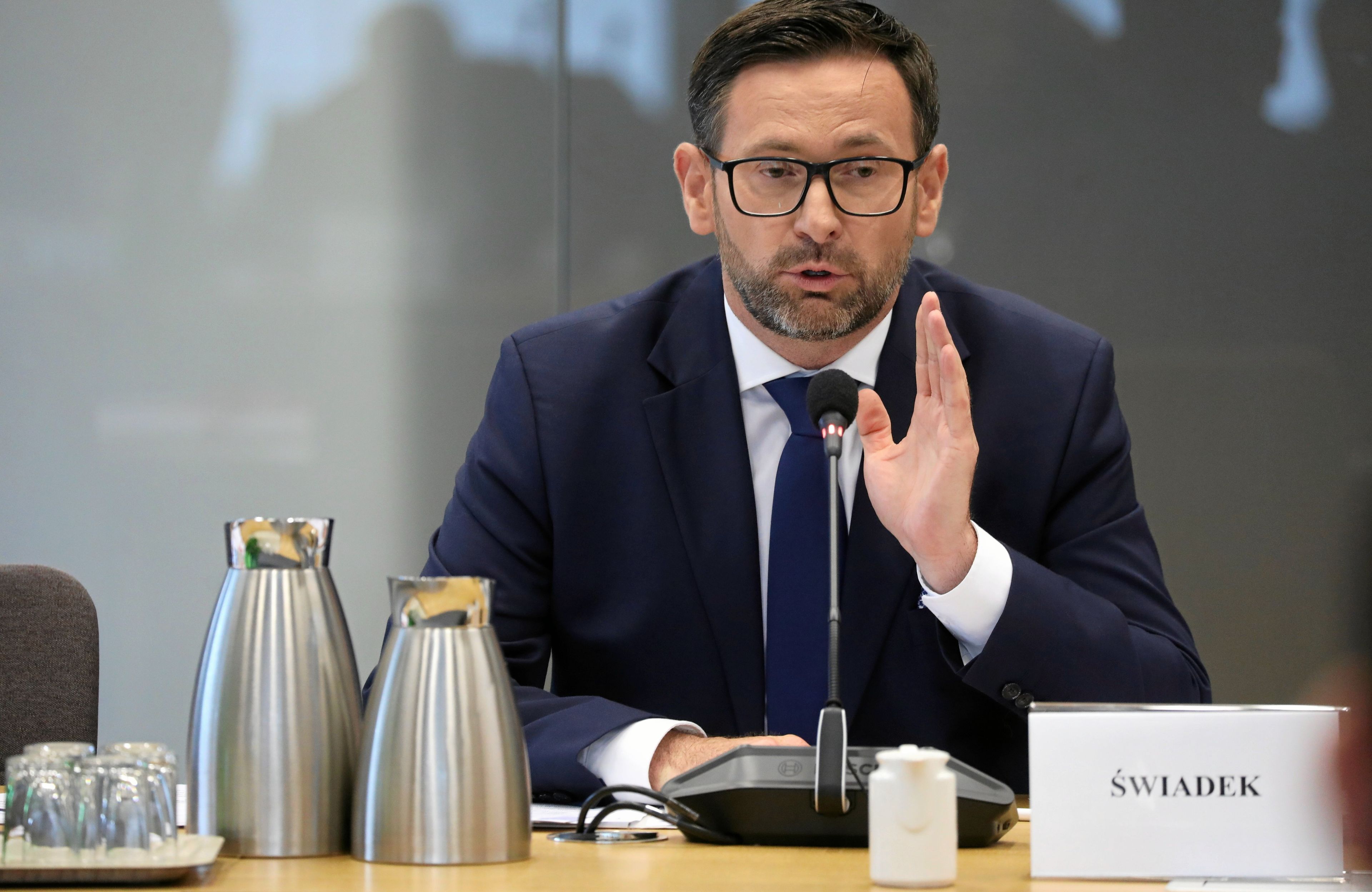 Mężczyzna w okularach podnosi prawą rękę przed twarzą