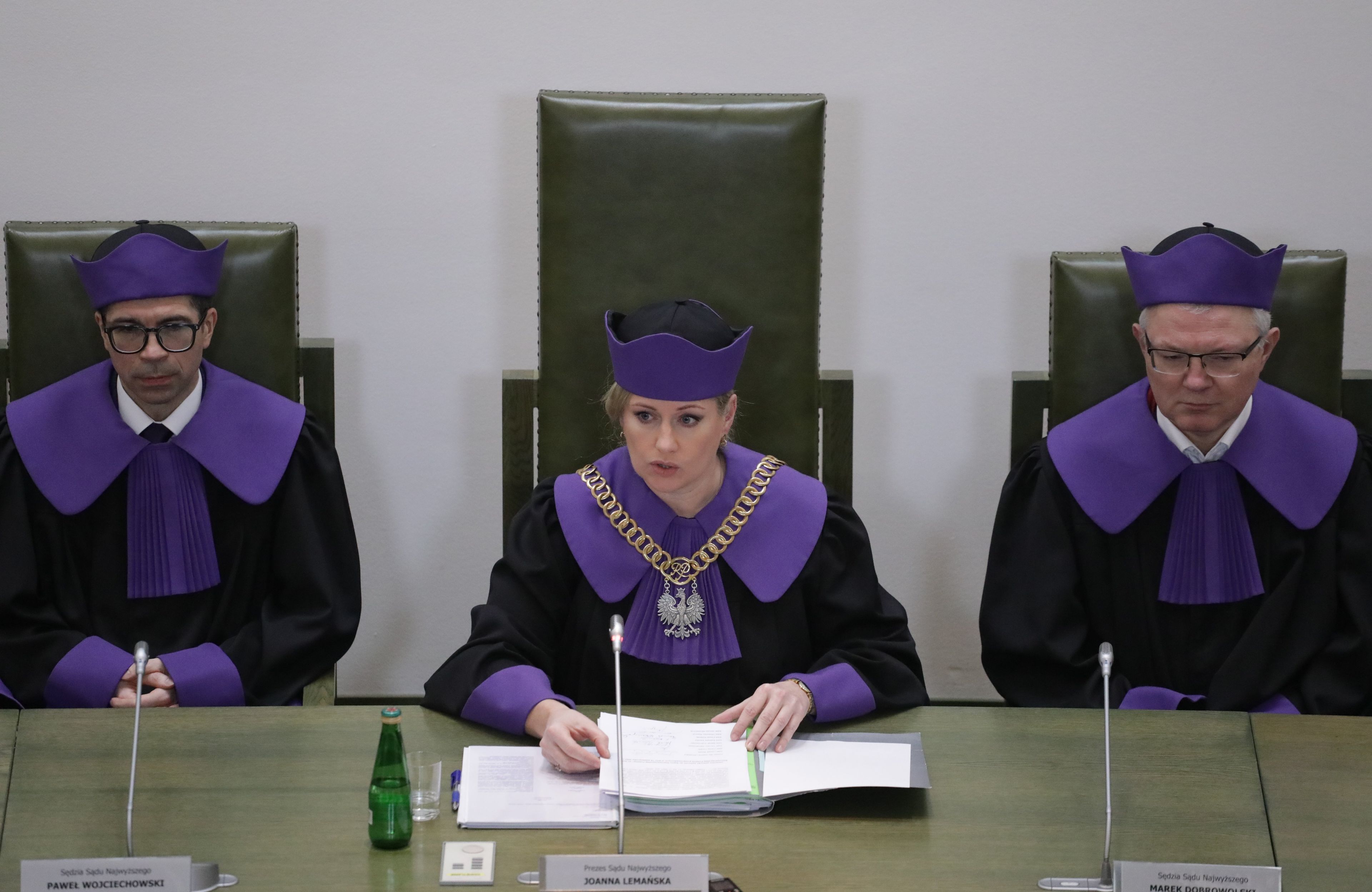 Na zdjęciu widzimy trójkę sędziów w Izbie Kontroli Nadzwyczajnej. Siedzą za zielonym stołem, ubrani są w togi z fioletowymi połami. W środku siedzi Joanna Lemańska, prezes Izby