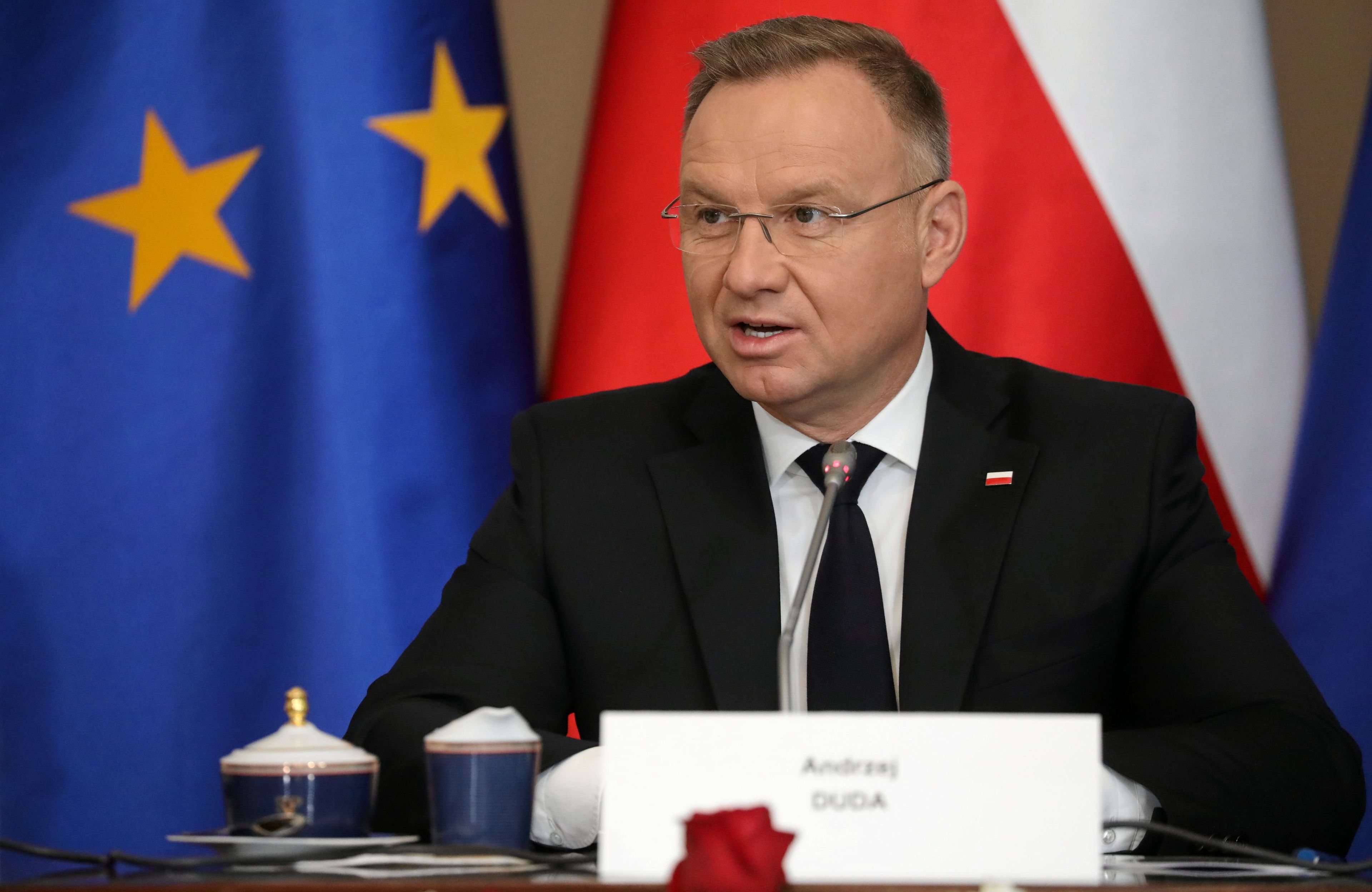 prezydent w okularach siedzi na tle flagi polski i ue