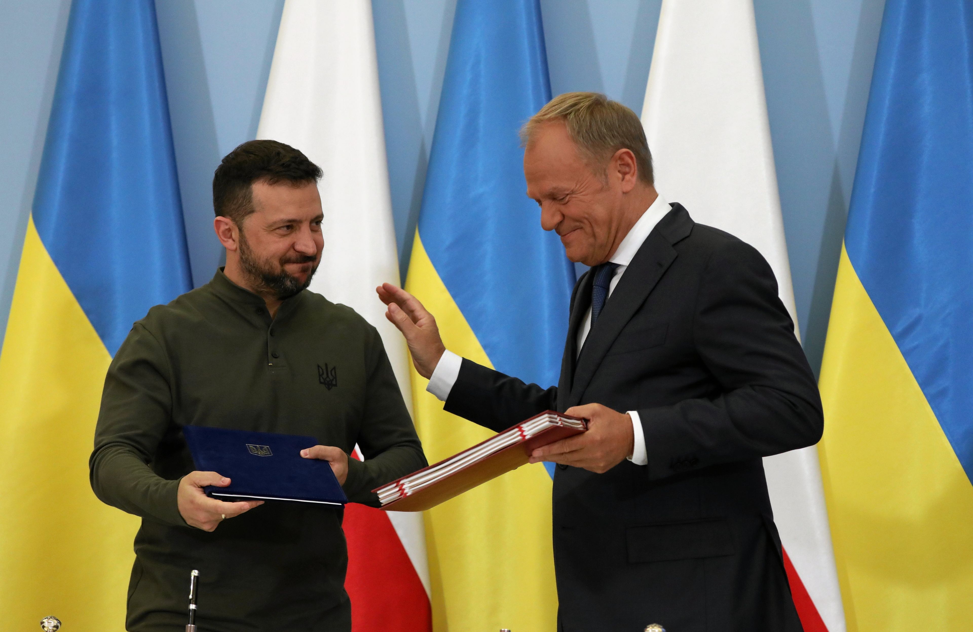 Premier Polski i premier Ukrainy wymieniają dokumenty, są uśmiechnięci, w tle polska i ukraińska flaga