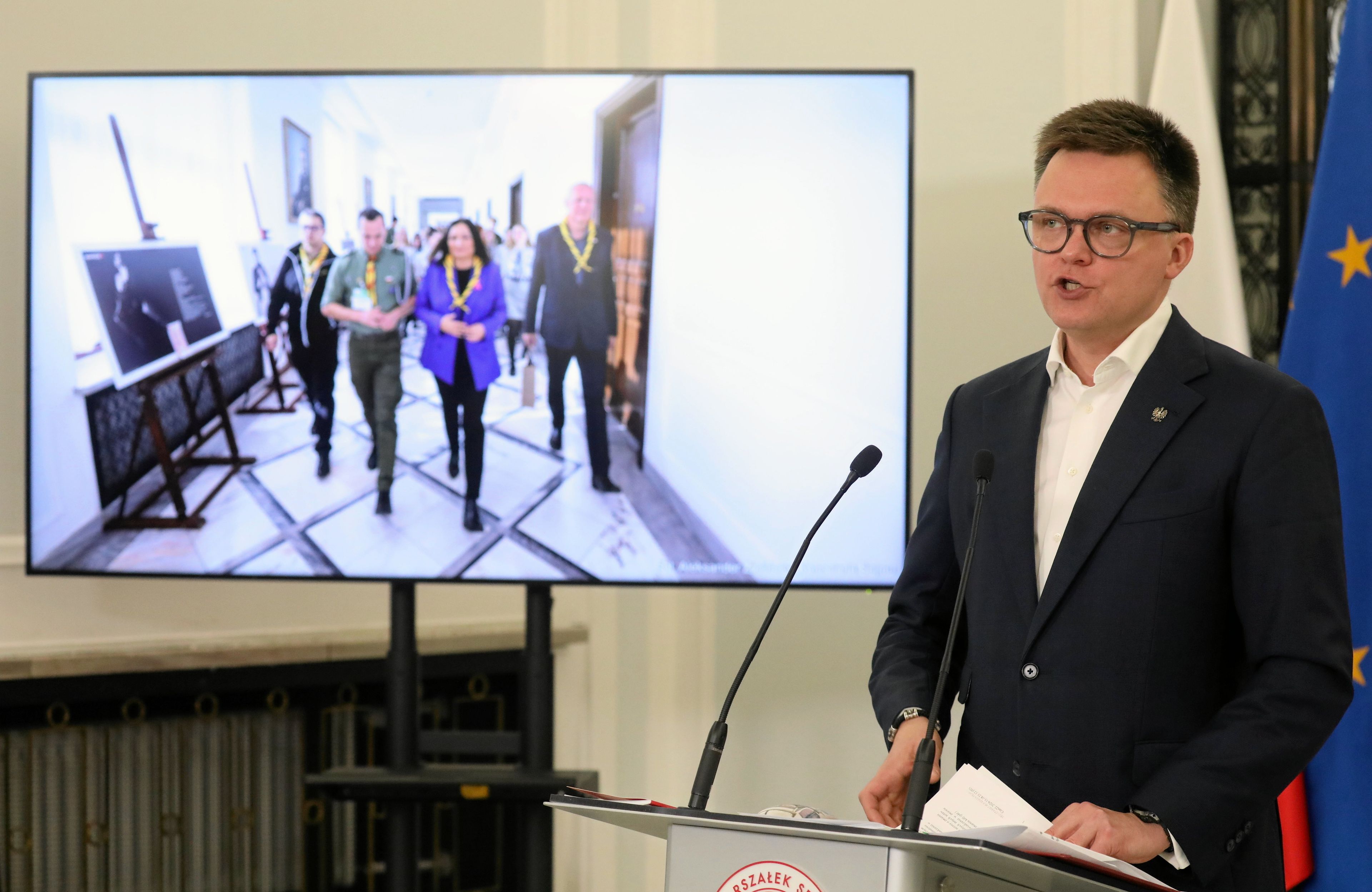 hołownia stoi przed mikrofonem