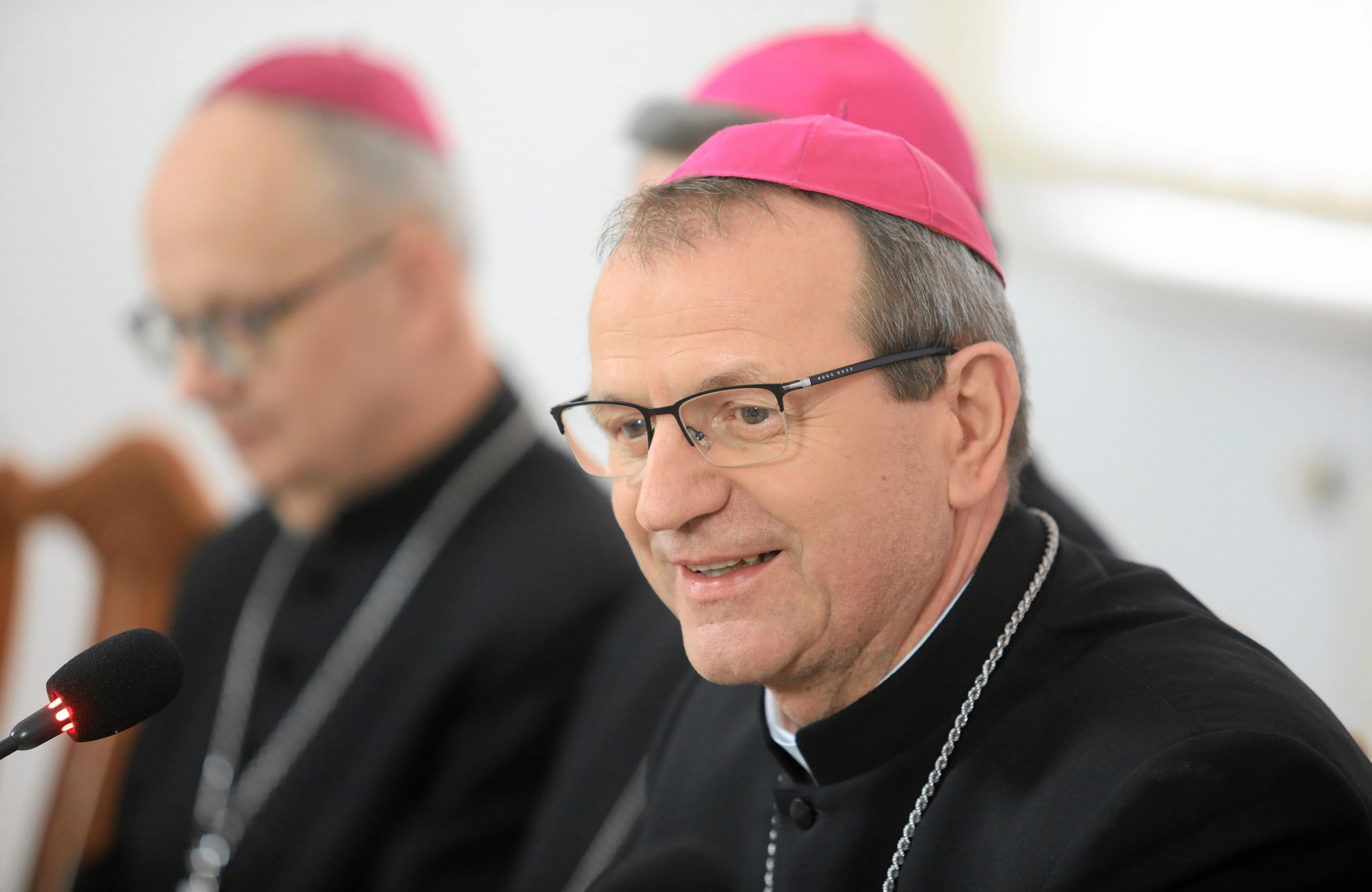 Mężczyzna, ksiądz, w okularach, siedzi, ma strój biskupi