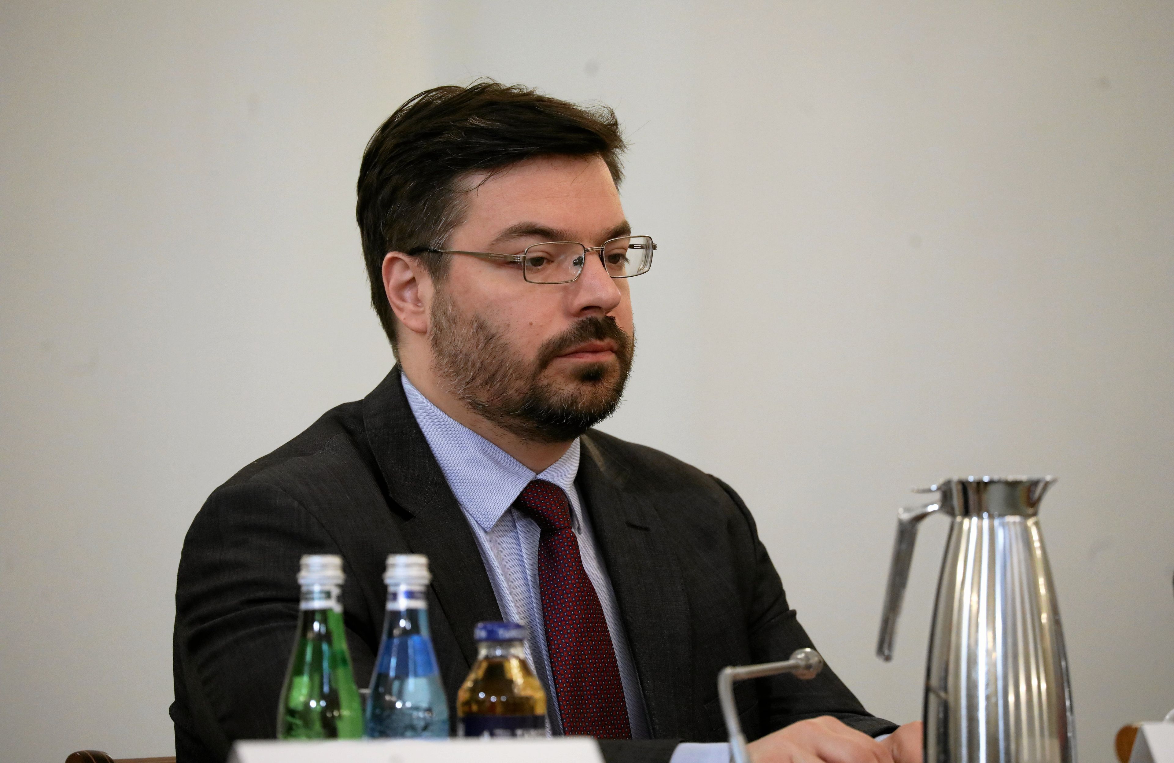 Stanisław Tyszka - mężczyzna w ciemnych włosach, brodzie i okularach, siedzi za stołem konferencyjnym