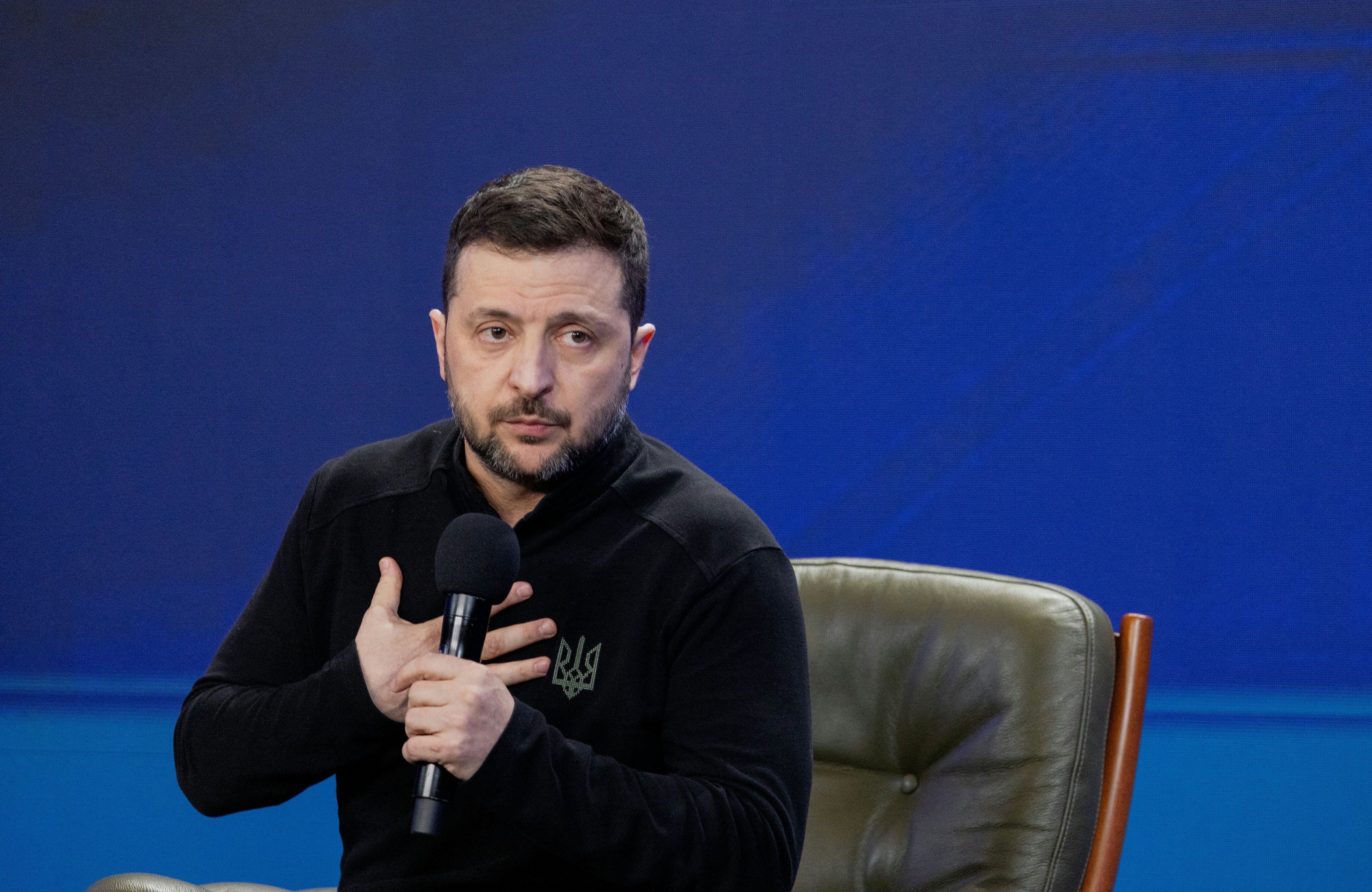 Wołodymyr Zełenski trzyma mikrofon i rękę na sercu
