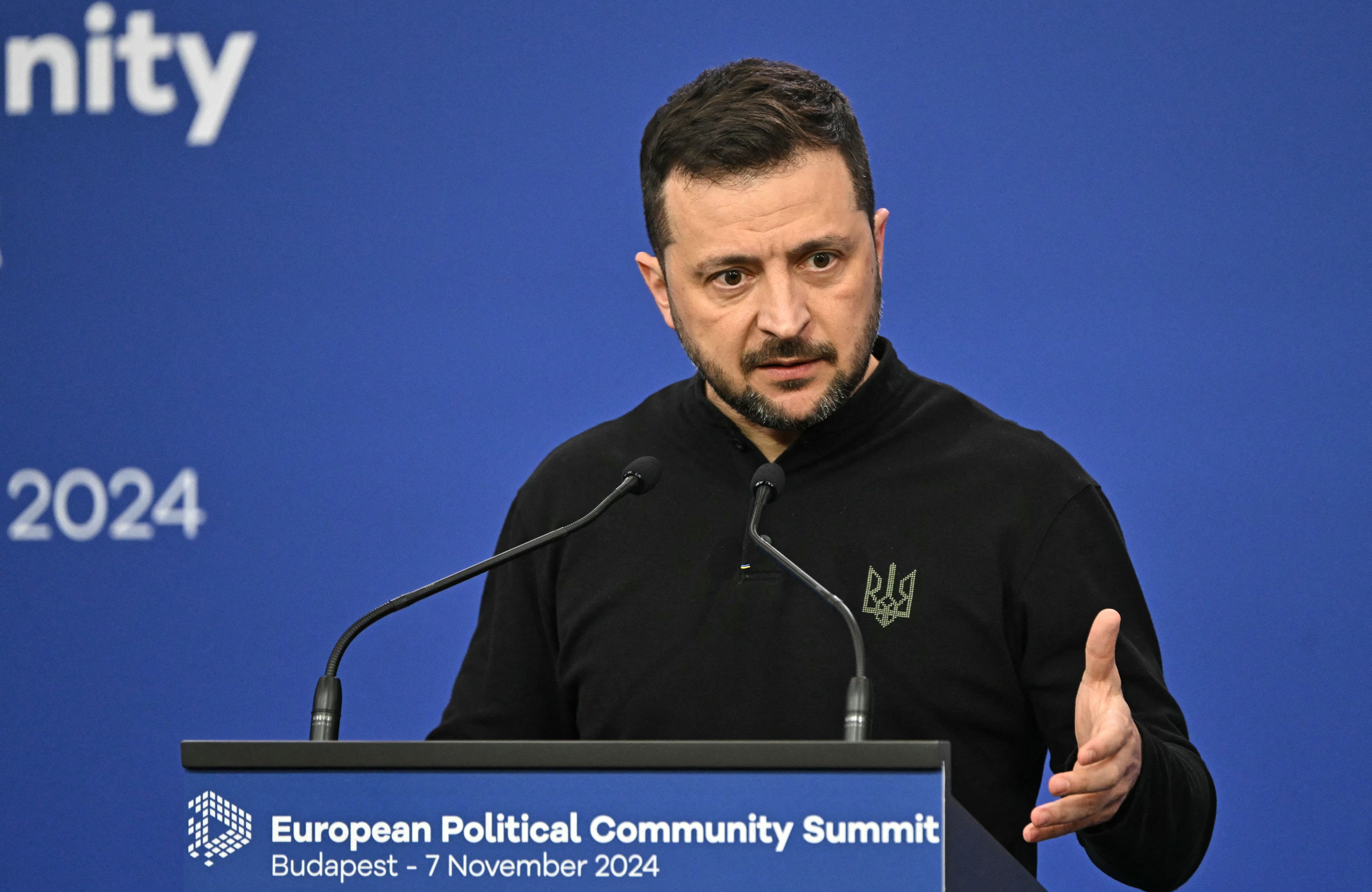 Na zdjęciu jest mężczyzna ok. 45 lat. Ma czarne krótkie włosy i brodę. Jest ubrany w czarną bluzę z wyhaftowanym tryzubem po prawej stronie. Przemiawia przez mikrofony.