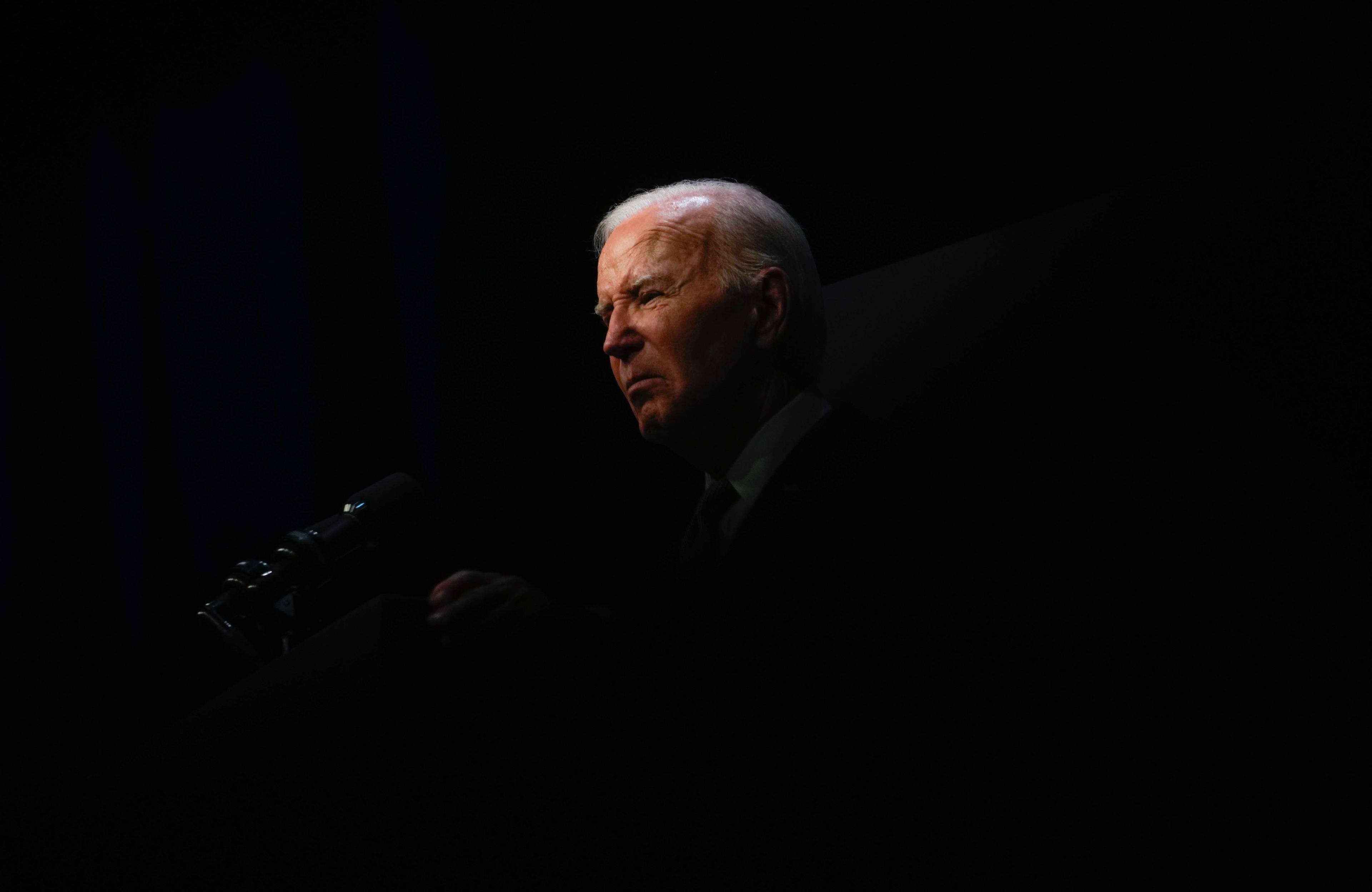 Joe Biden przemawia do mikrofonu, otoczony mrokiem